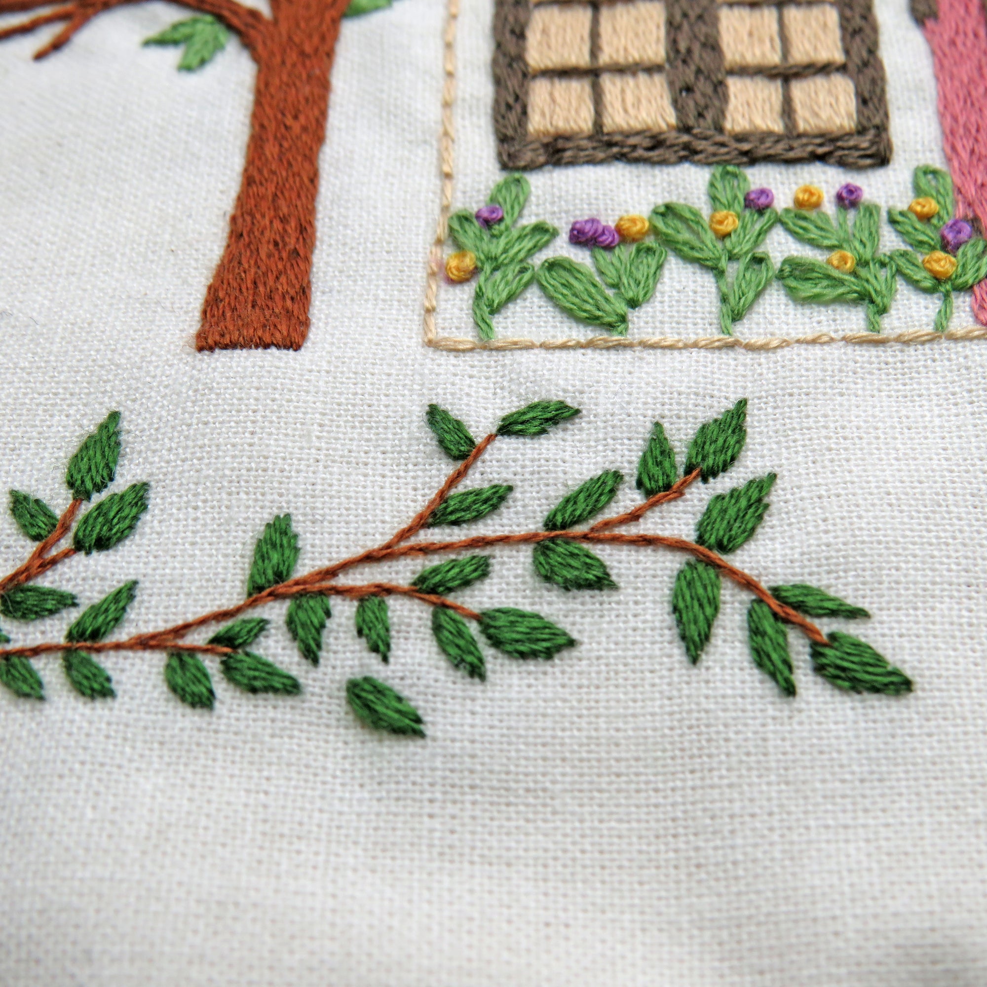 Embroidered scene with a house, tree, and garden on fabric