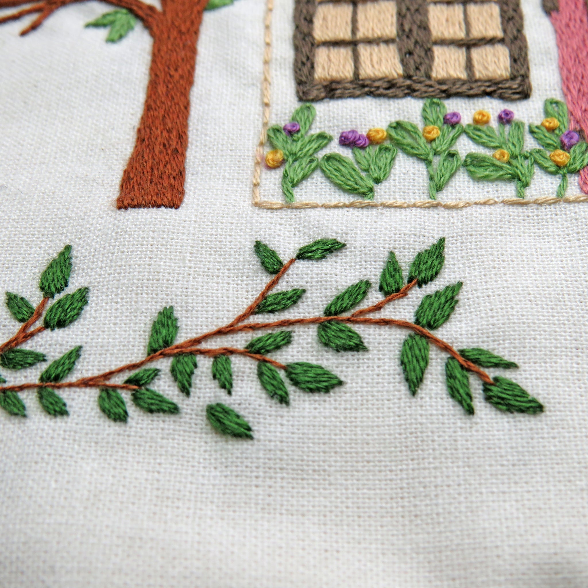 Embroidered scene with a house, tree, and garden on fabric