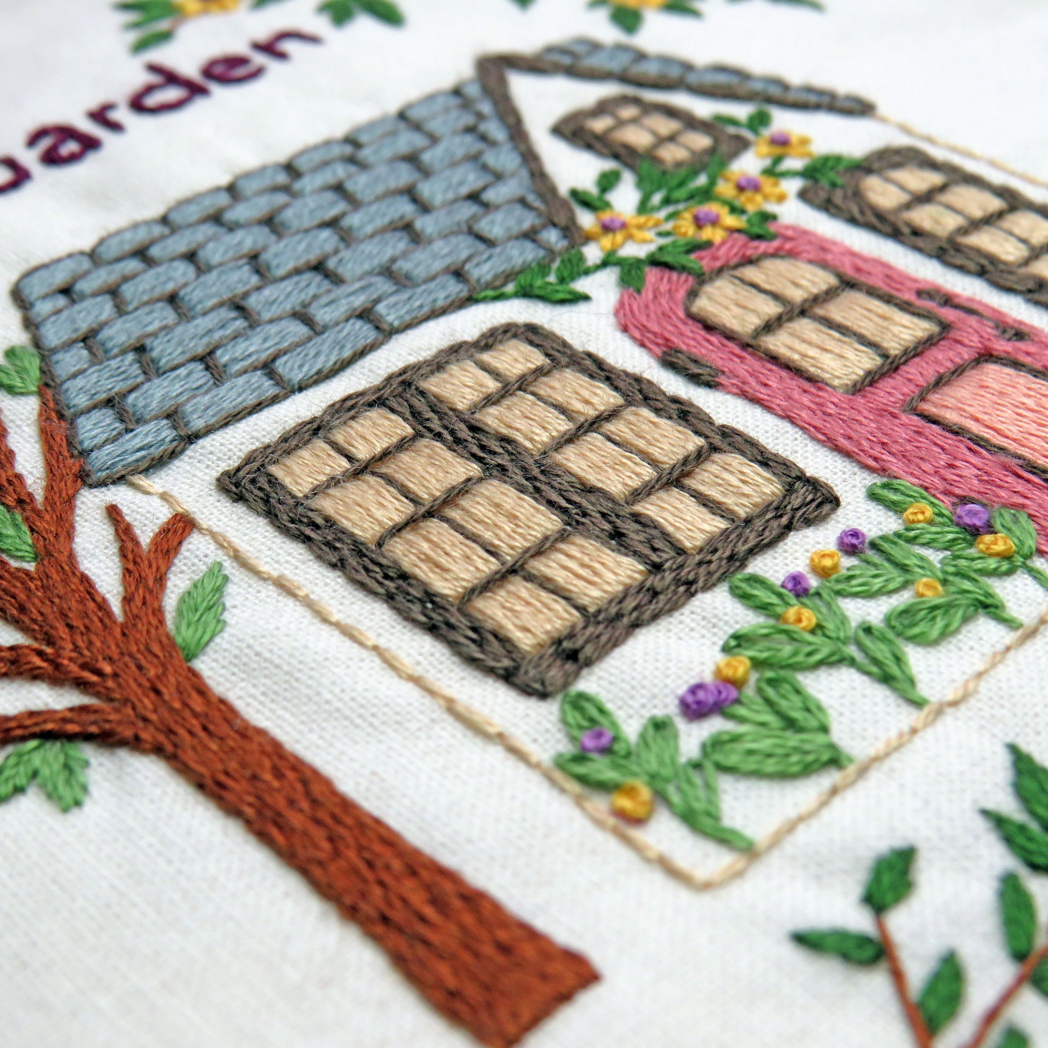 Embroidered design of a garden scene with houses and trees.