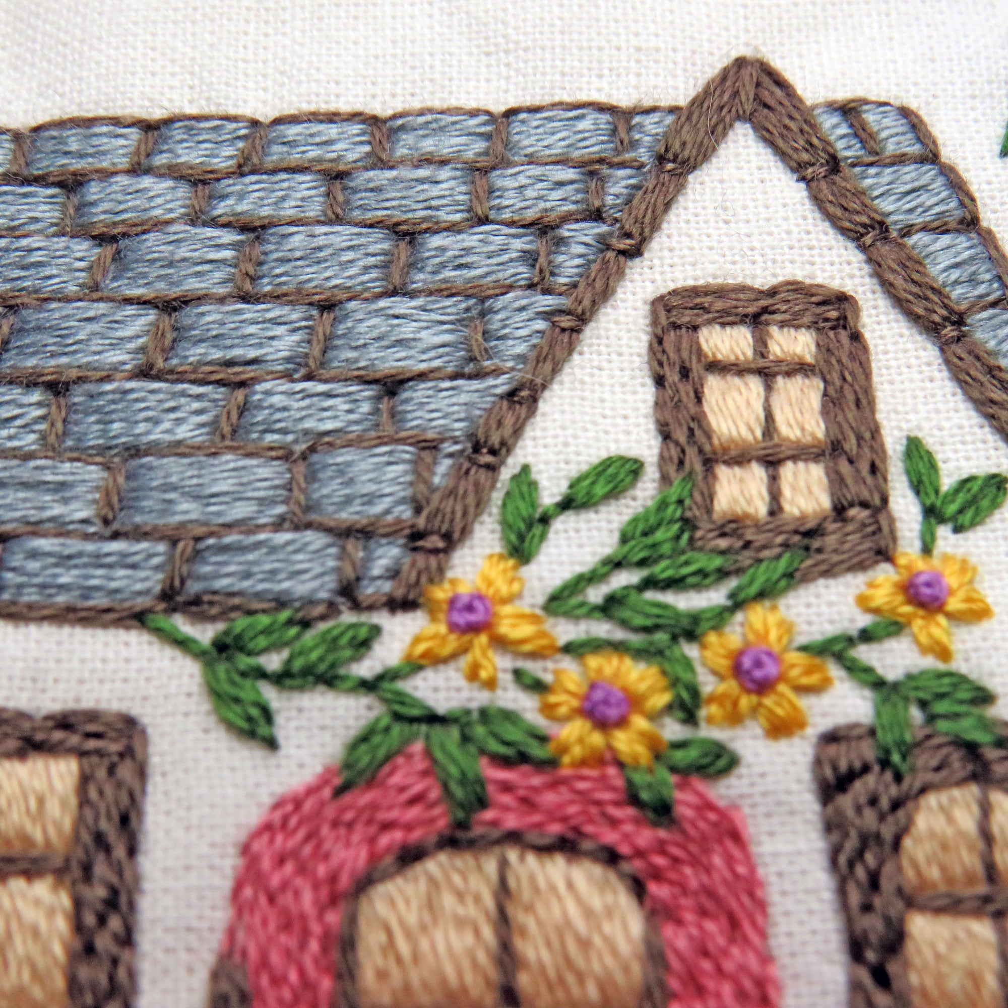 Embroidered design of a house with flowers and plants