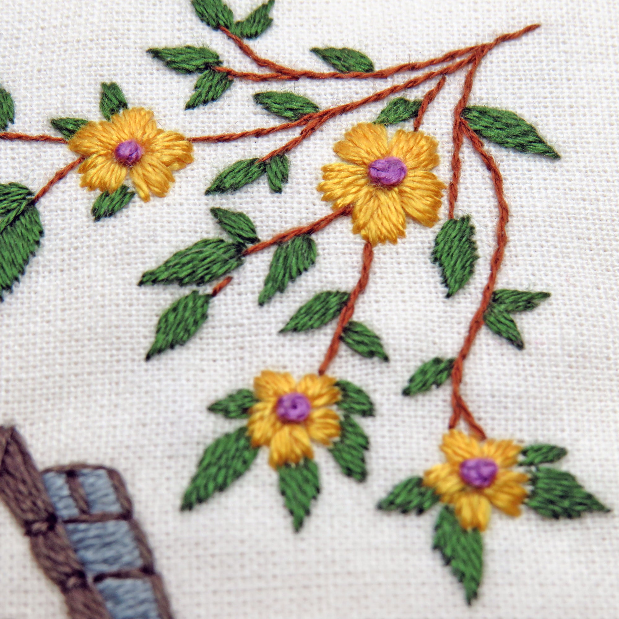 Embroidered design of yellow flowers with green leaves on a white fabric background.