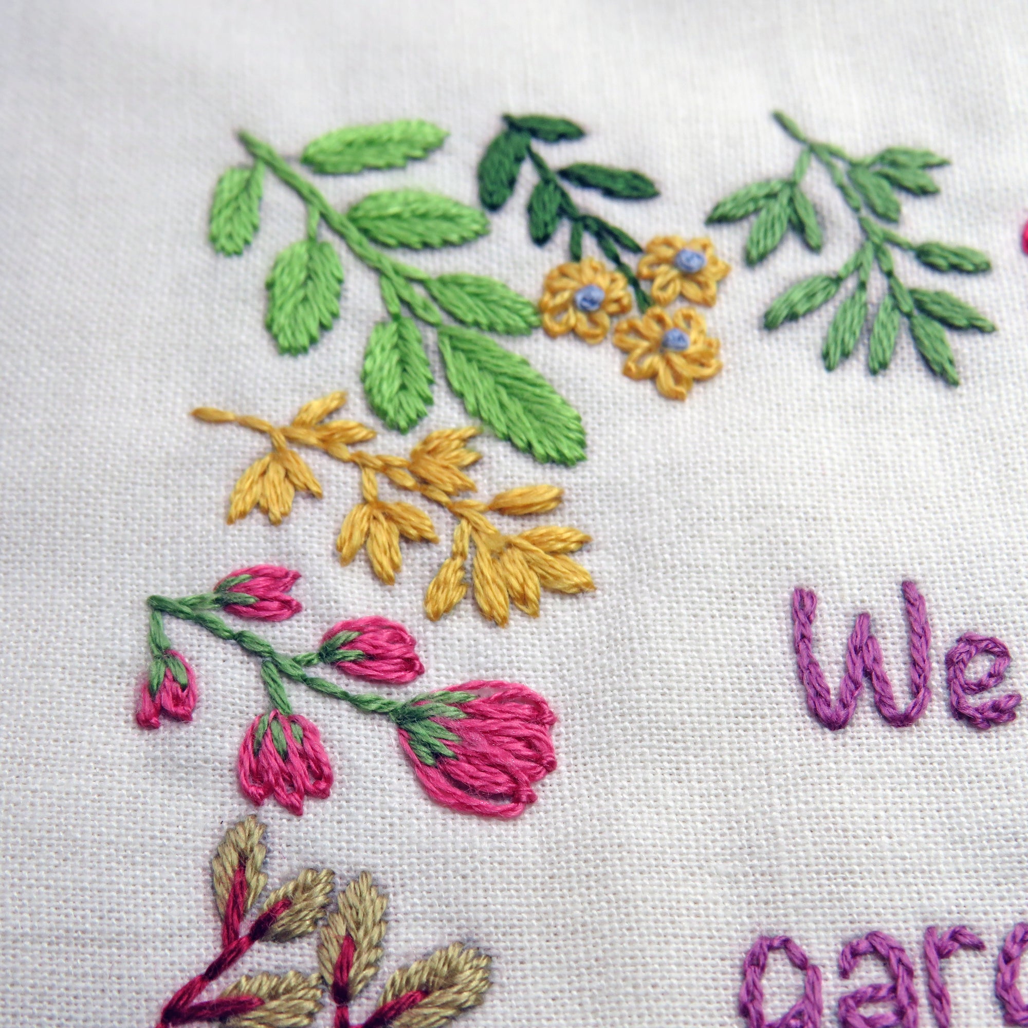 Embroidered floral design with leaves and flowers on a white fabric background.