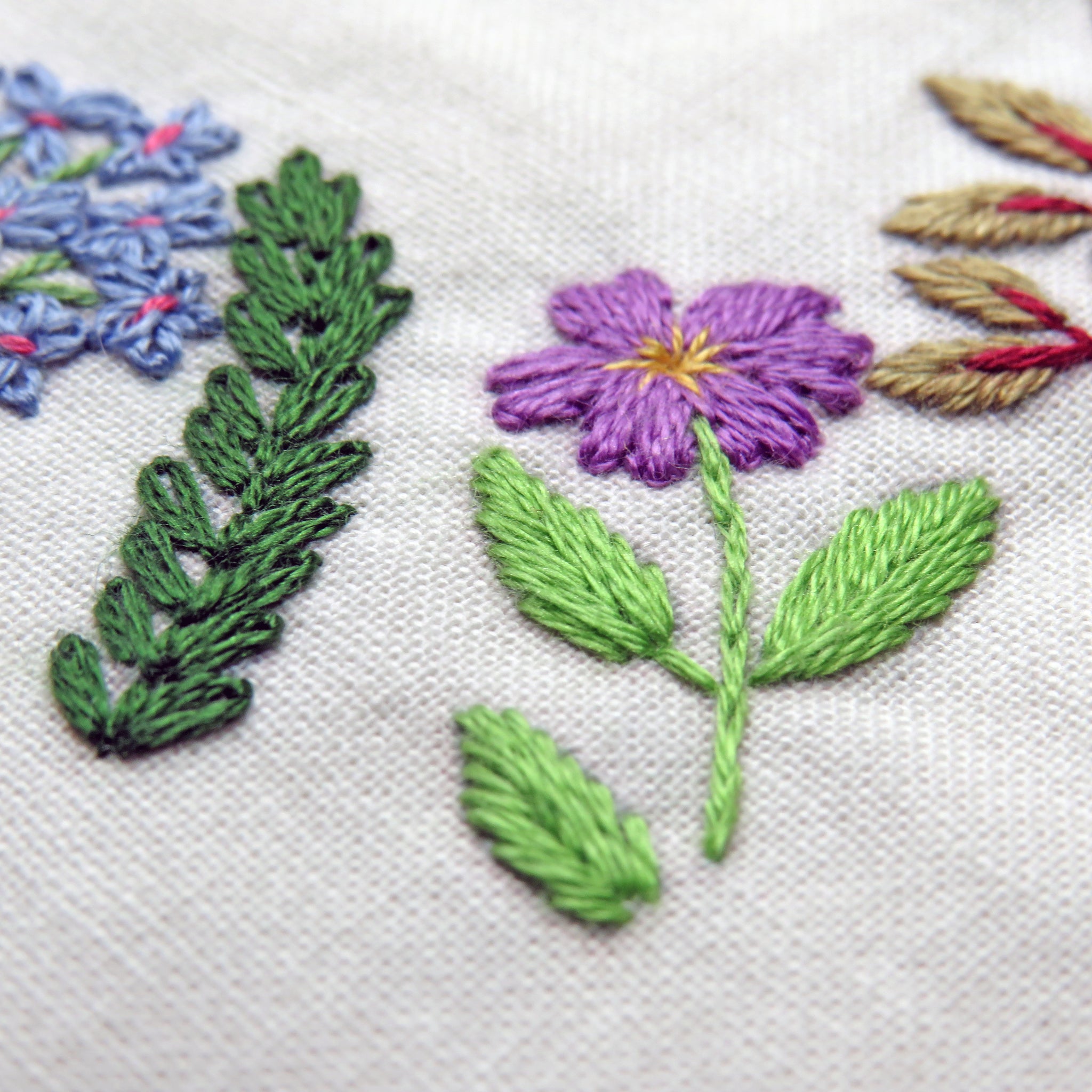 Embroidered floral design with purple flower and green leaves on a white fabric background