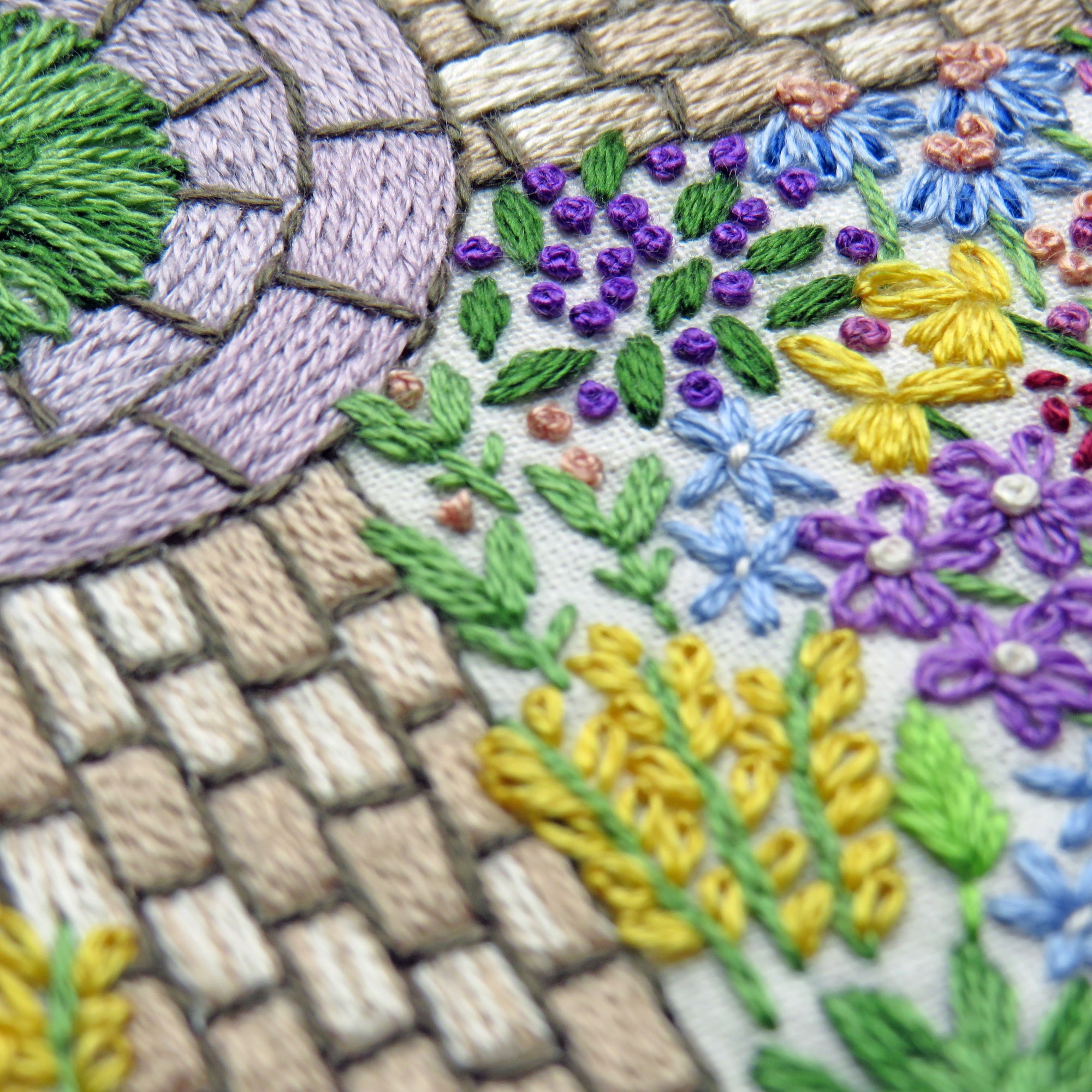 Close-up of embroidered floral pattern with green, purple, yellow, and blue colors.