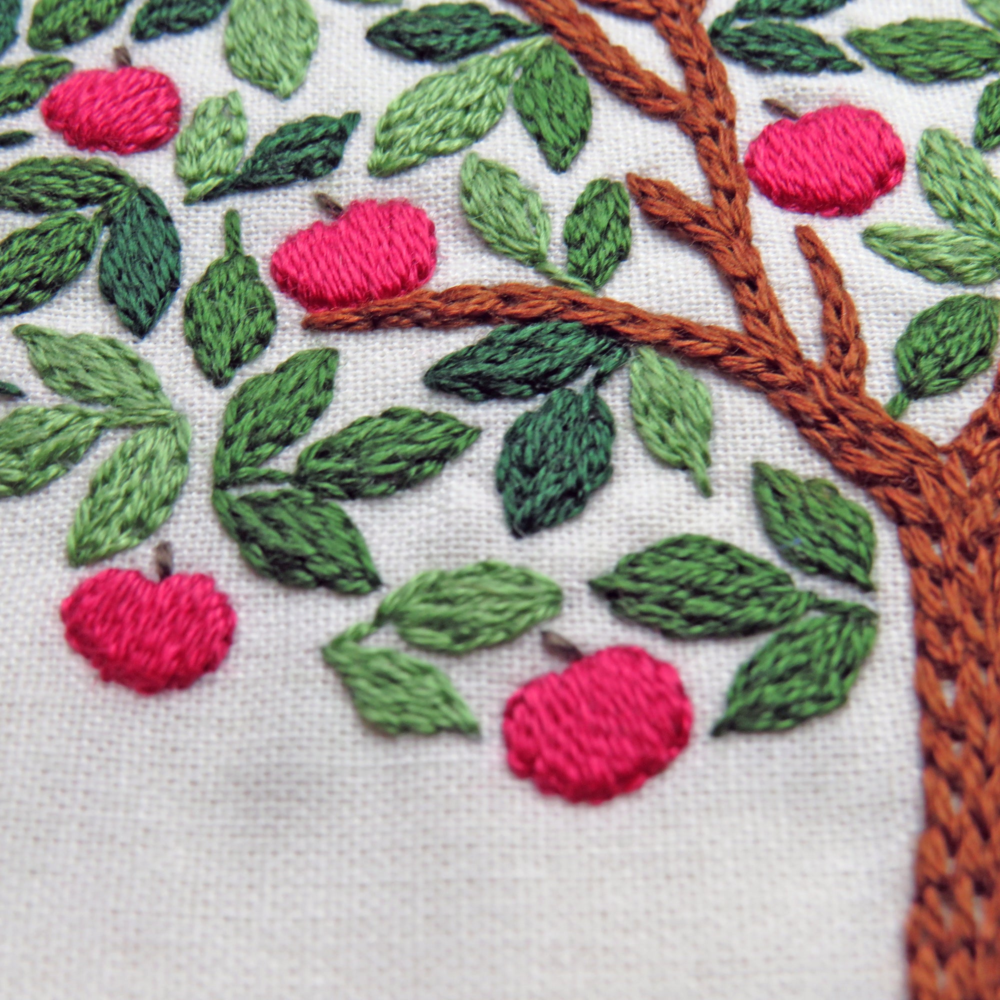 Embroidered design of an apple tree with red apples and green leaves on a white background.