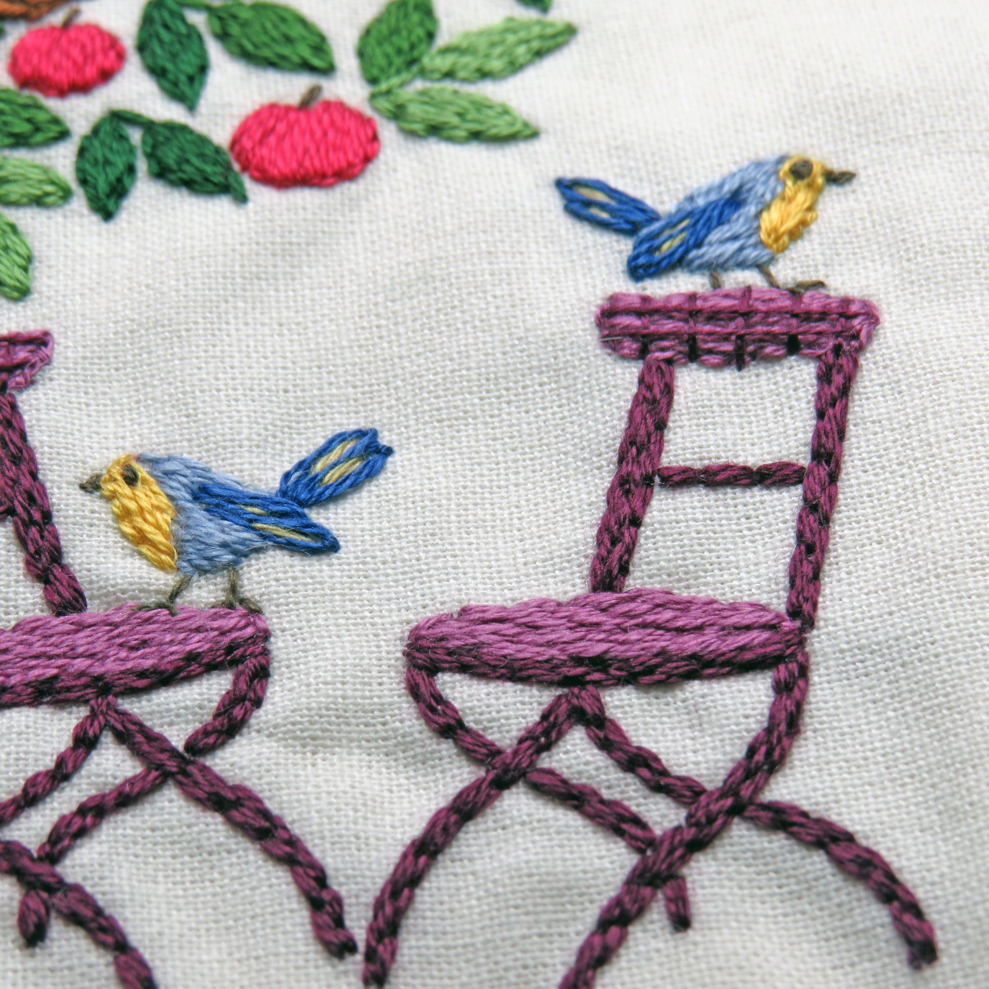 Embroidery of chairs and birds with colorful stitching on a white background