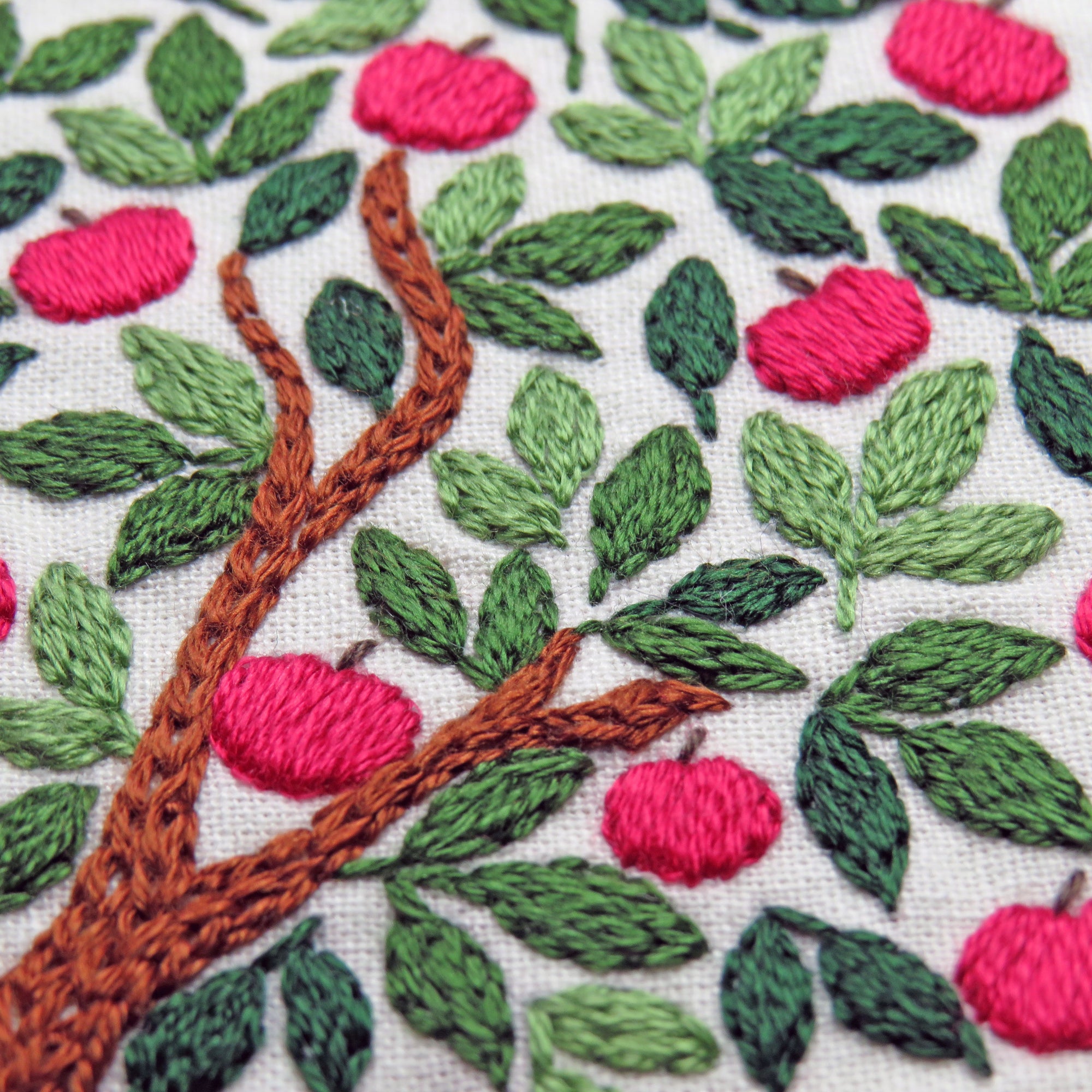 Embroidered pattern of a tree with red apples and green leaves on a white background