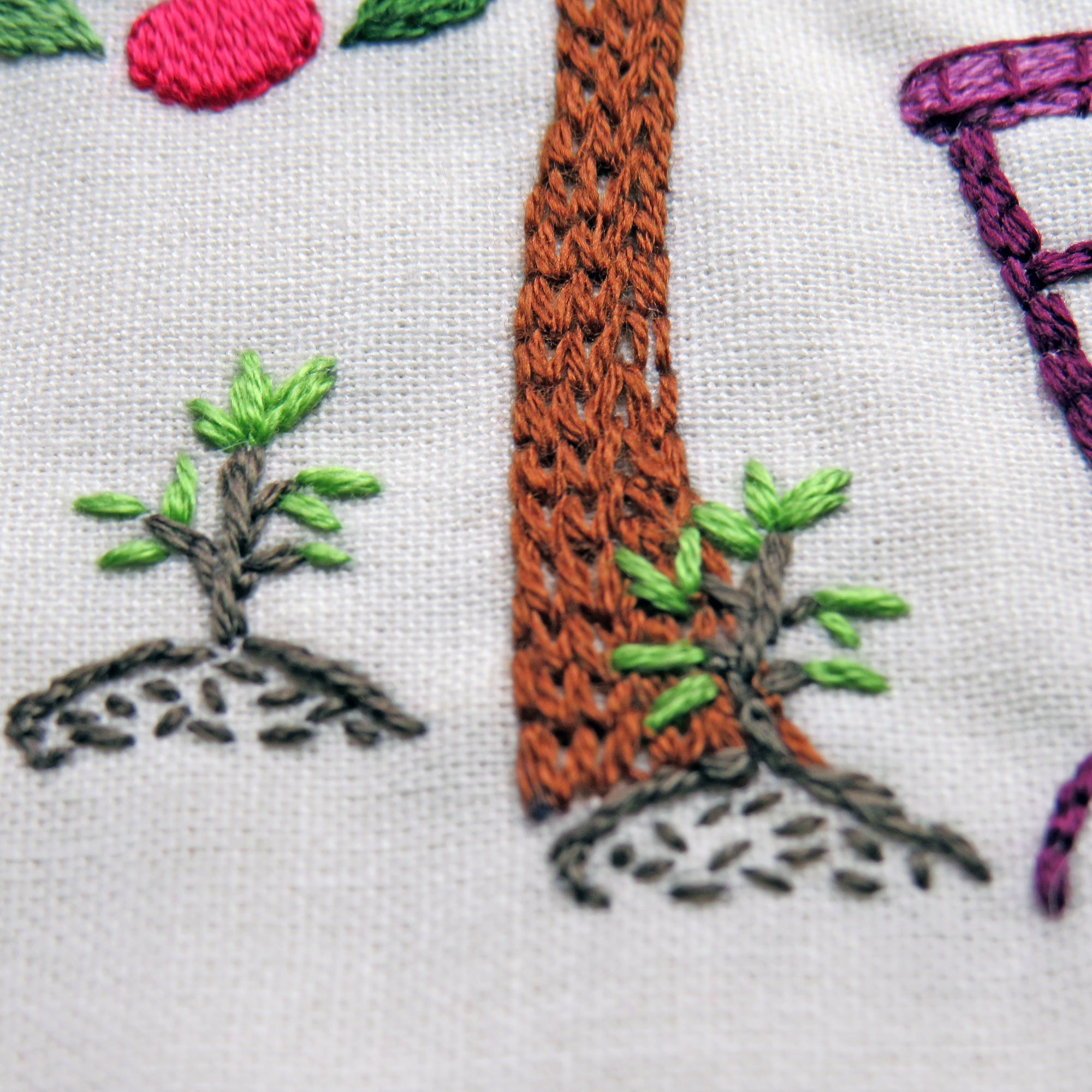 Embroidered scene with a broom, tree, and chair on fabric.