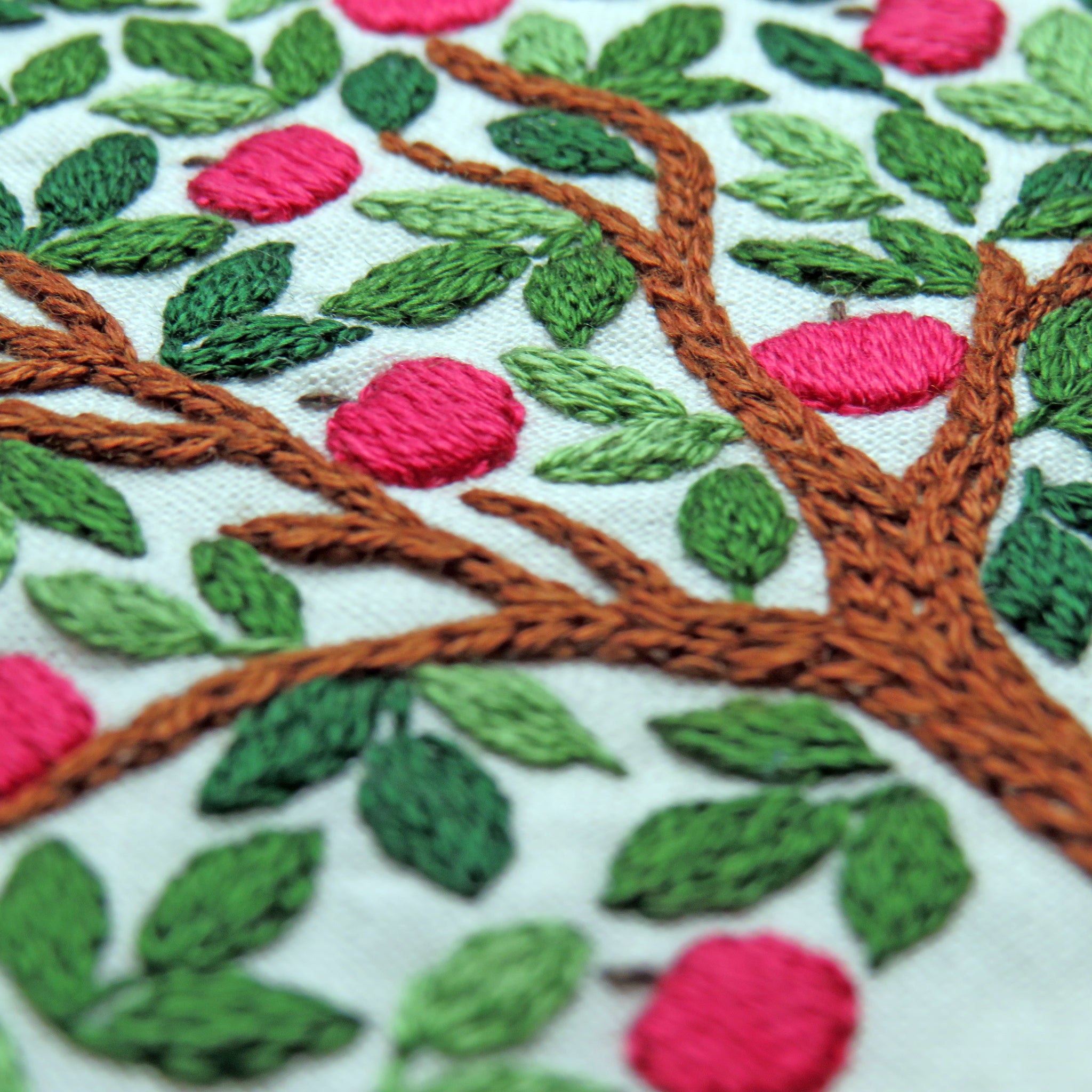 Embroidered design of a tree with pink flowers and green leaves on a white background