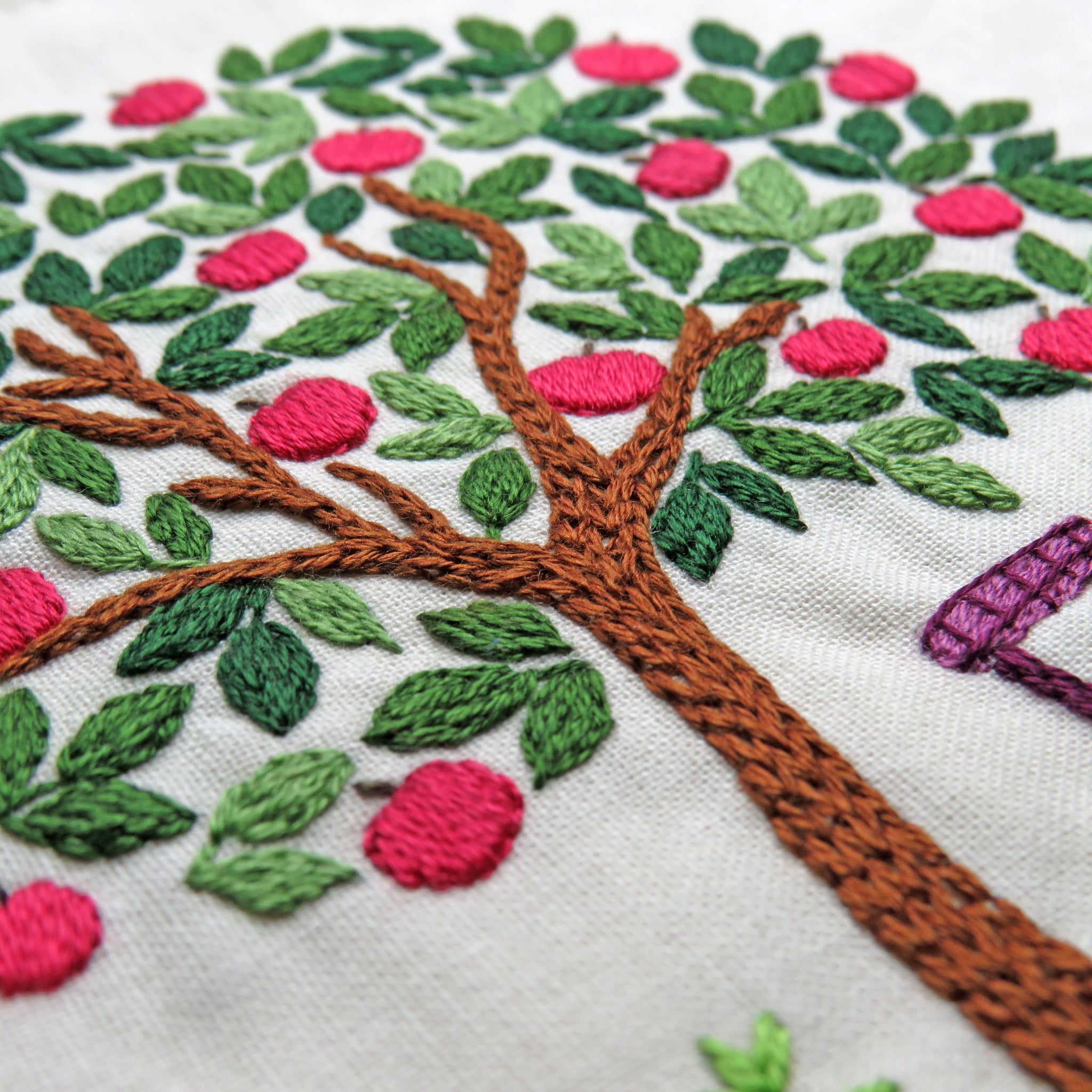 Embroidered tree design with pink flowers and green leaves on a white background
