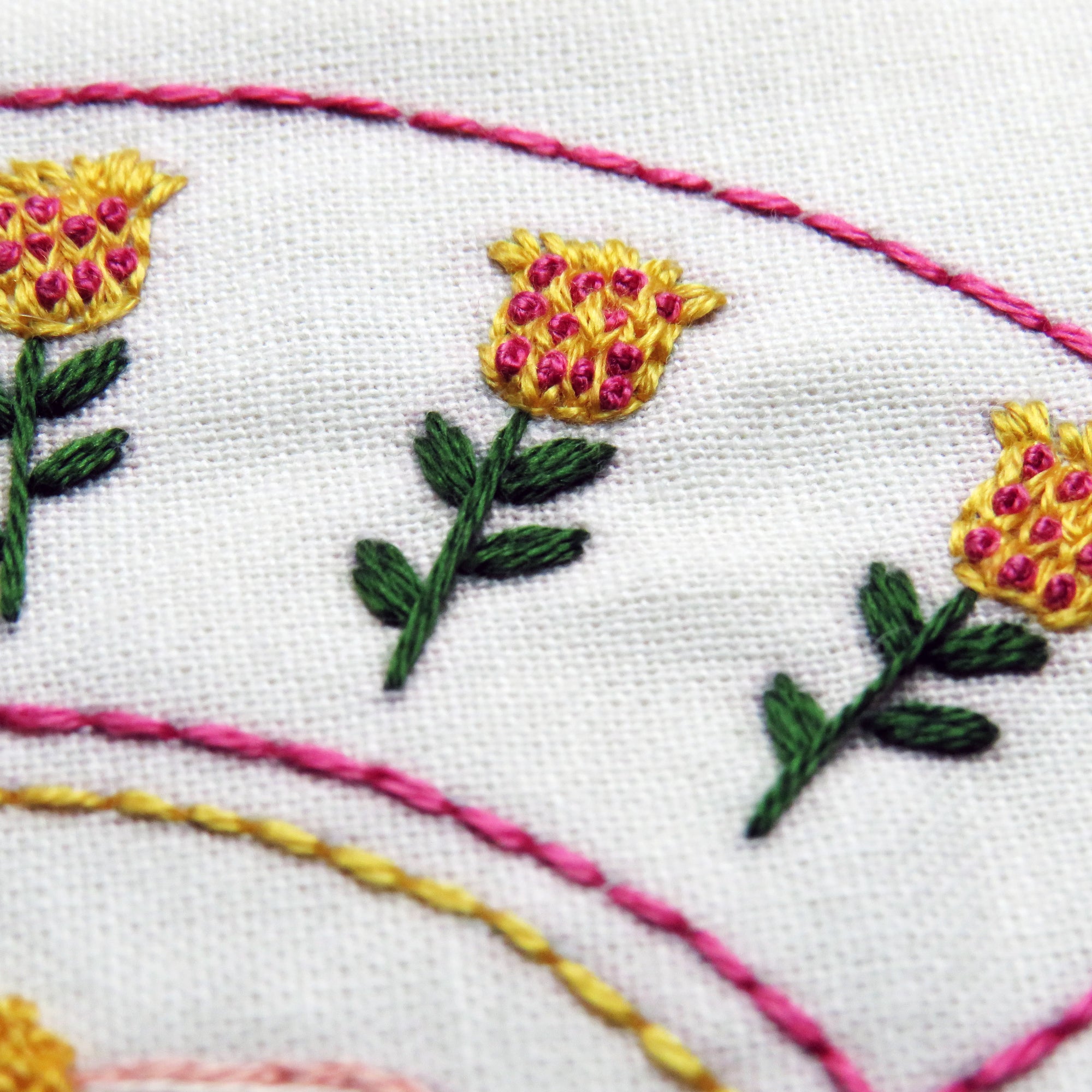 Embroidered flowers with pink centers and green leaves on white fabric.