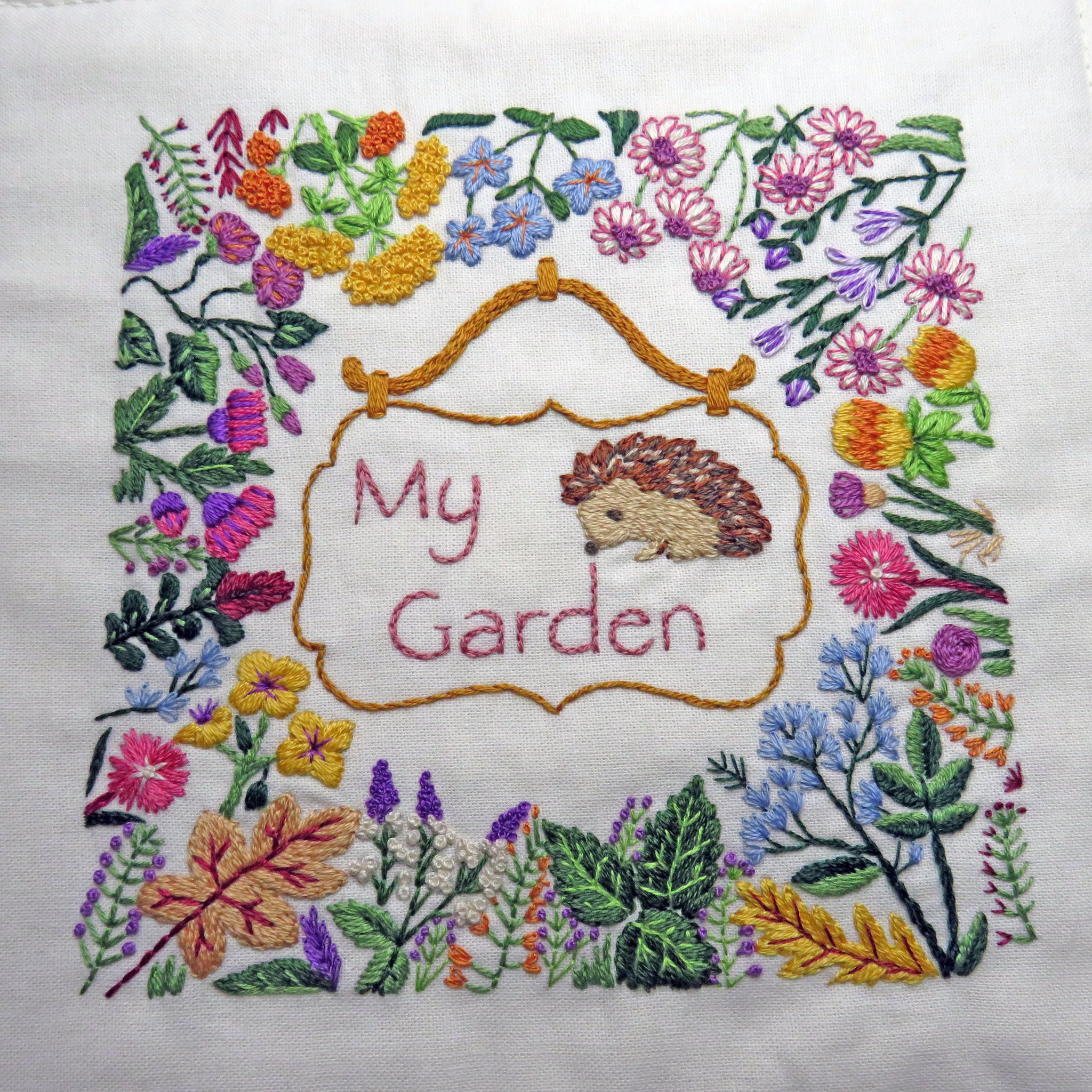 Embroidery of a hedgehog and floral design with 'My Garden' text on a white background