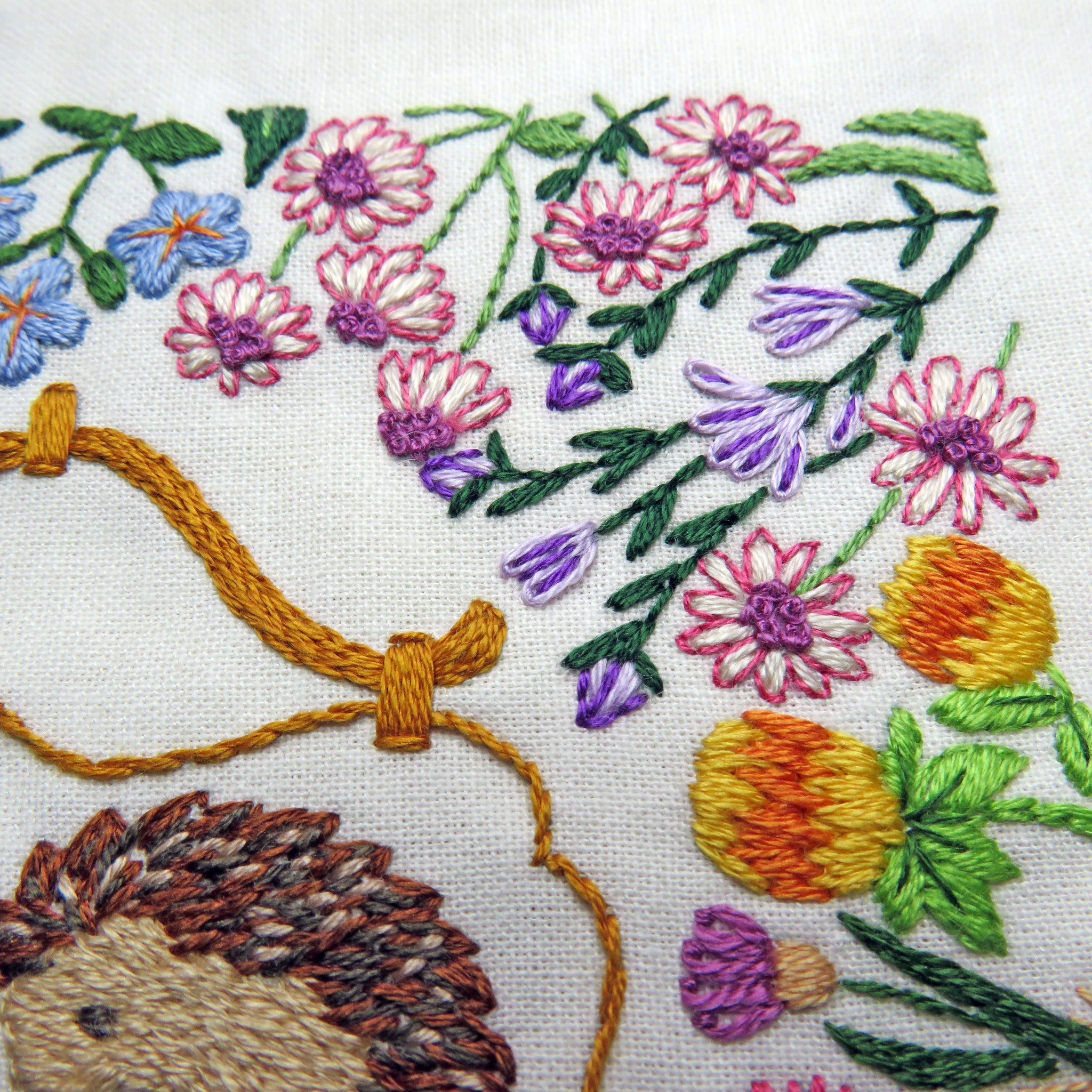 Embroidery of a hedgehog and flowers on white fabric