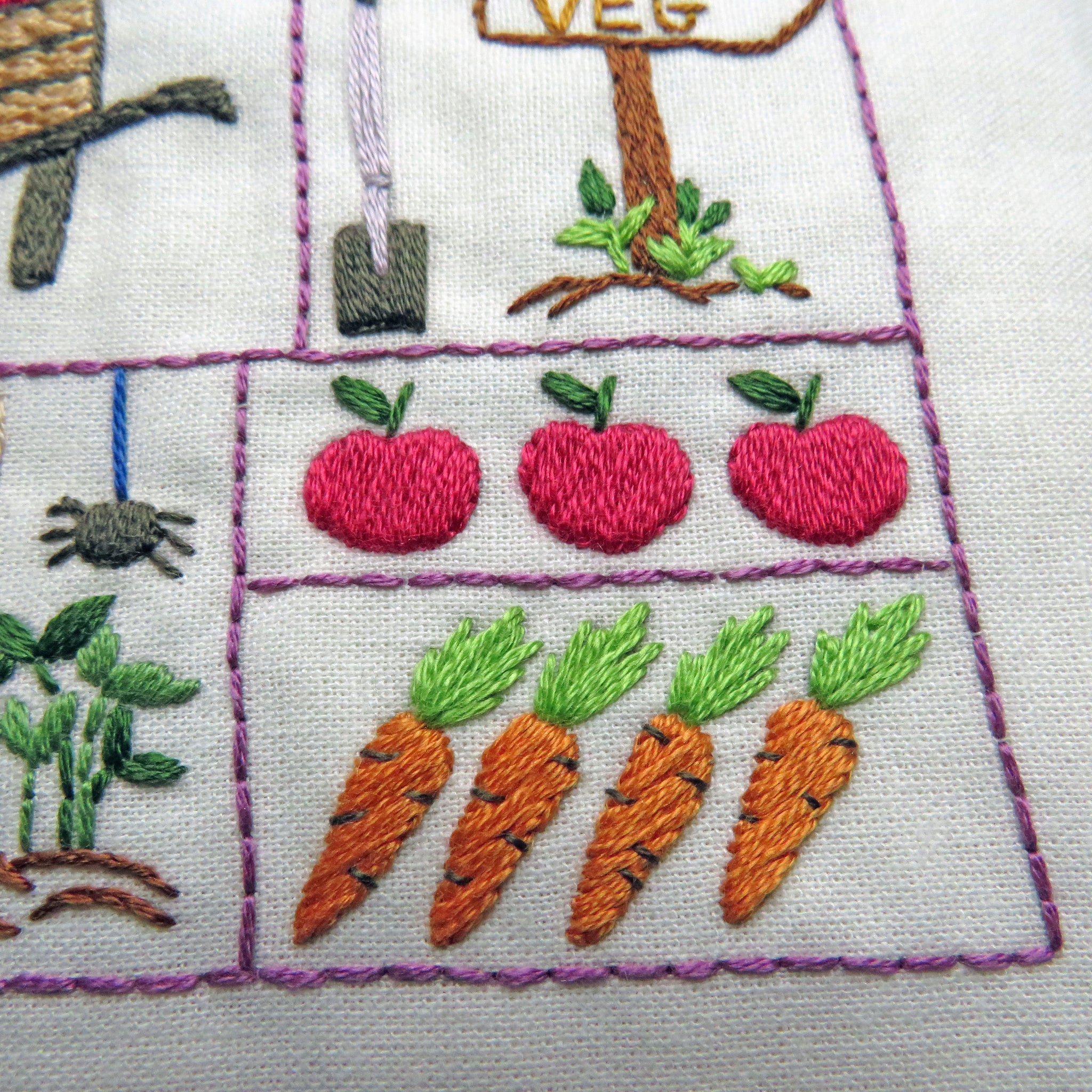Embroidered design of apples and carrots on a white fabric background