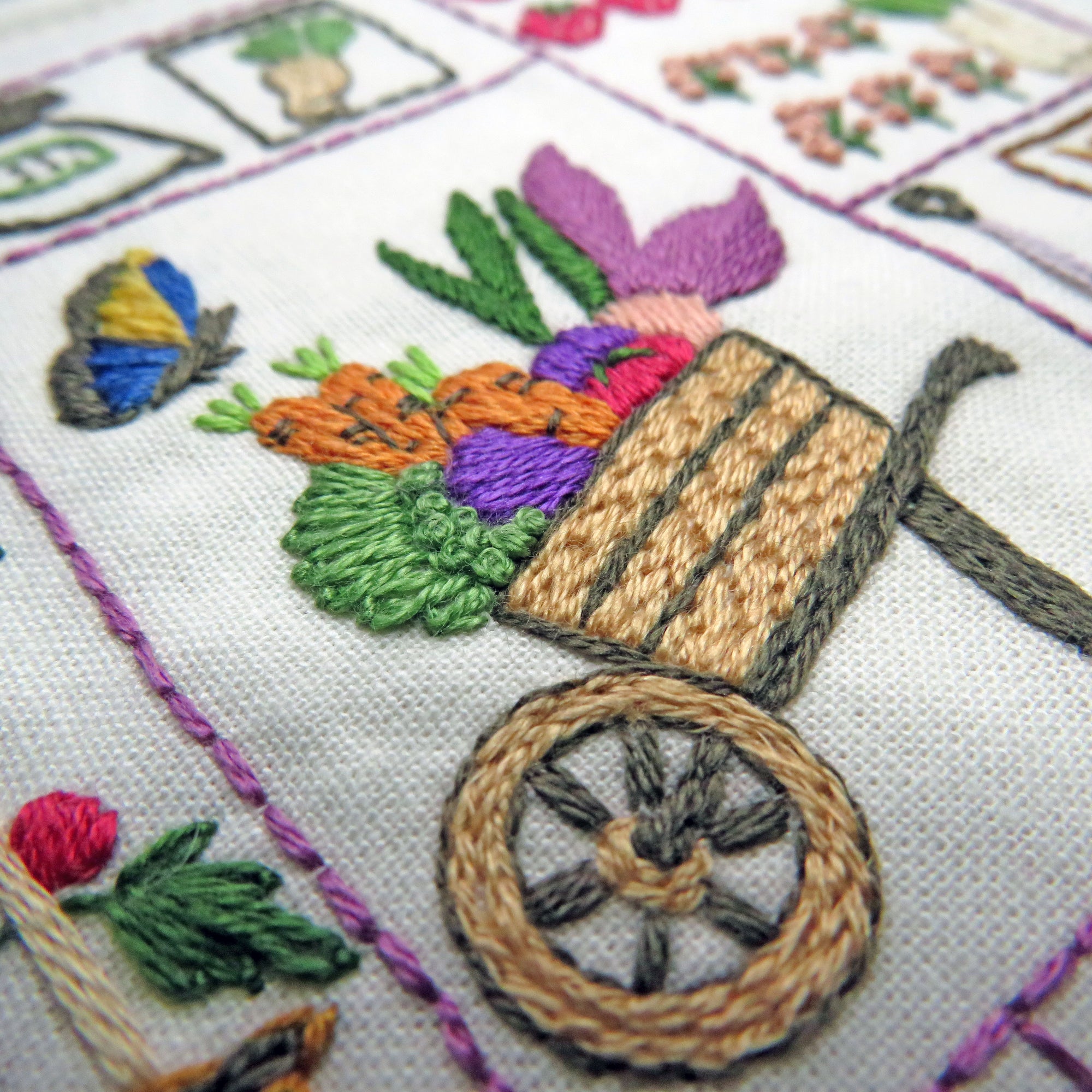 Embroidered design of a wheelbarrow with vegetables on a white fabric background