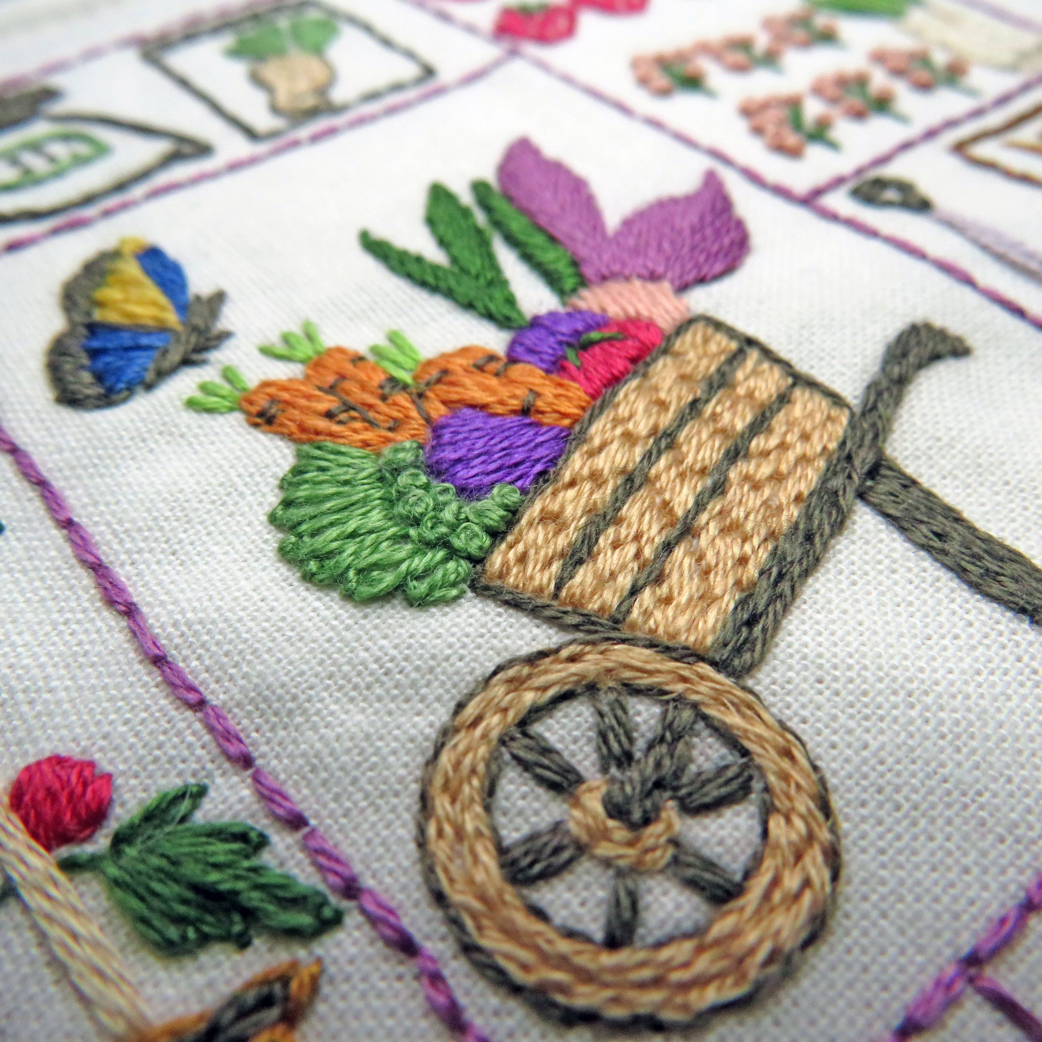 Embroidered design of a wheelbarrow with vegetables on a white fabric background