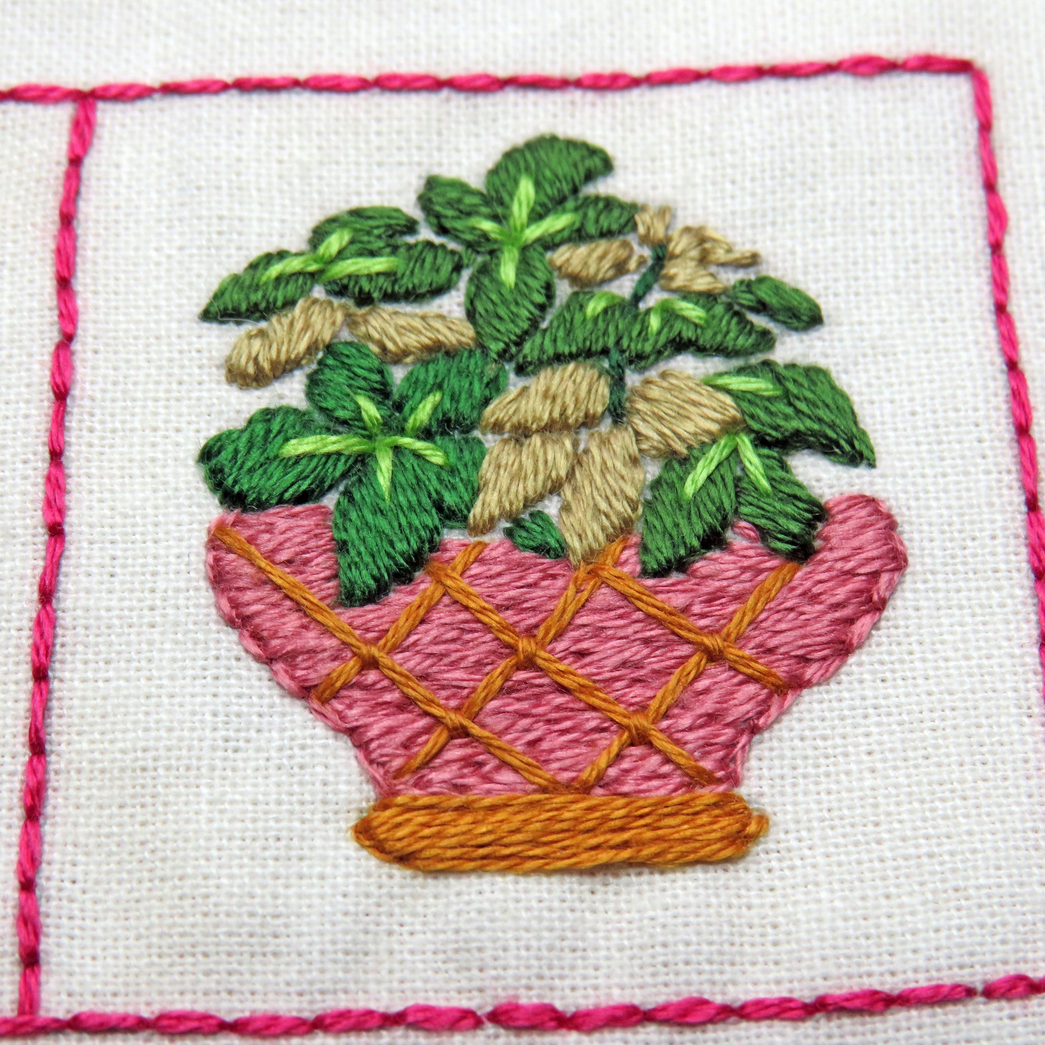 Embroidered design of a potted plant with pink pot on white fabric.