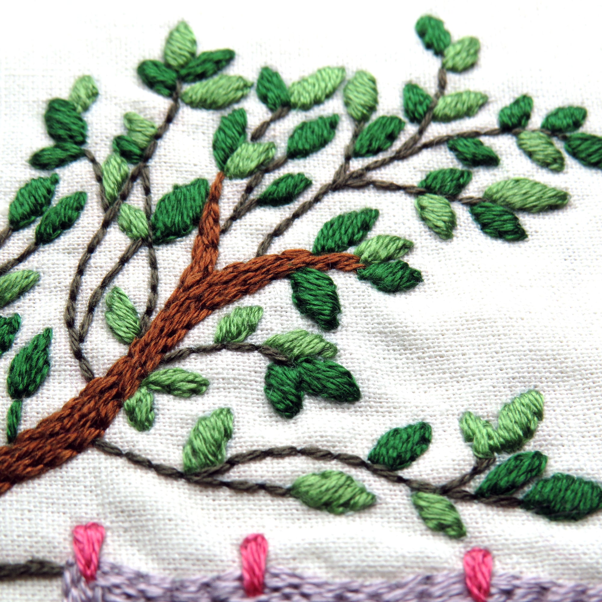 Embroidered tree design with green leaves and brown branches on a white background