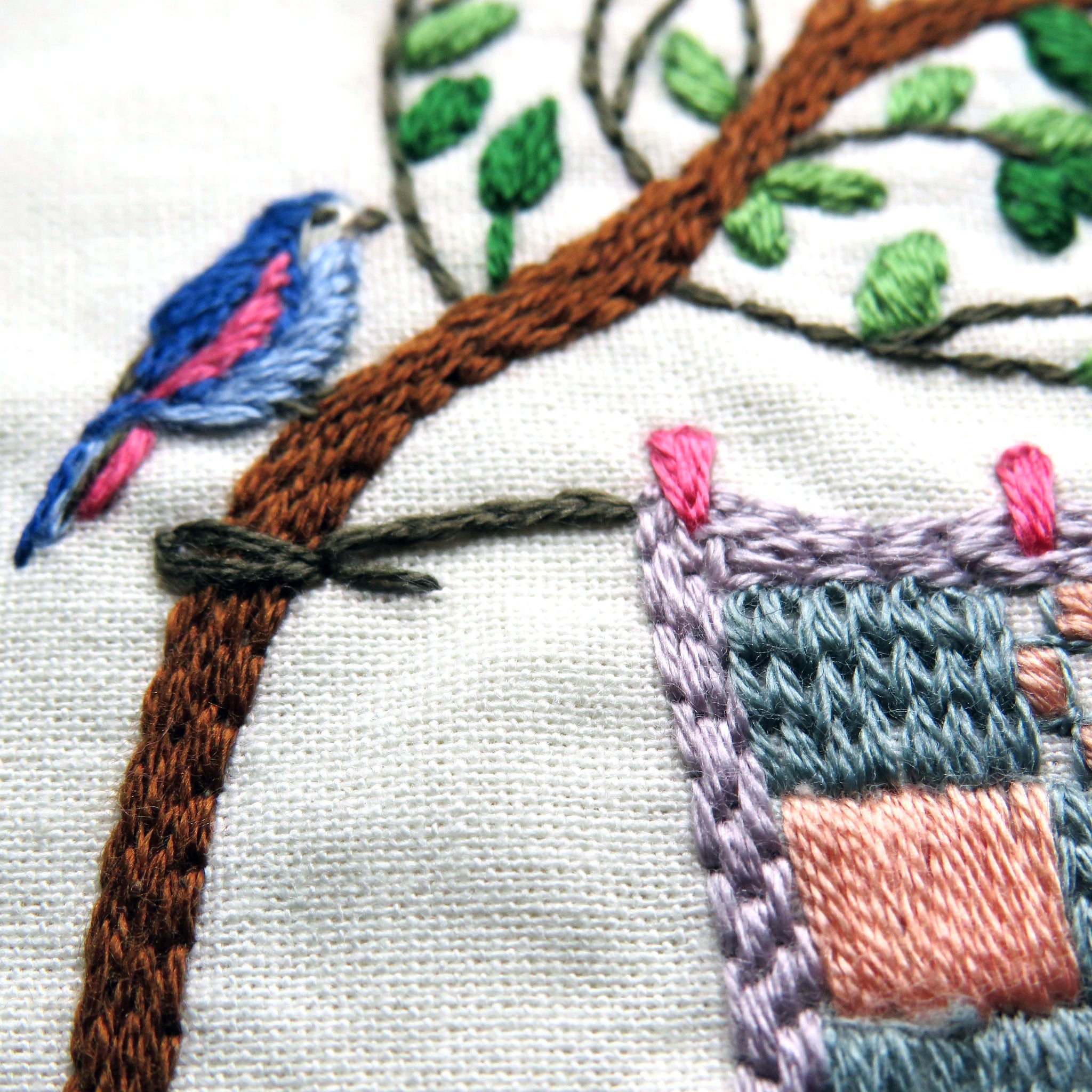 Embroidery of a bird on a branch with a quilted design in the background