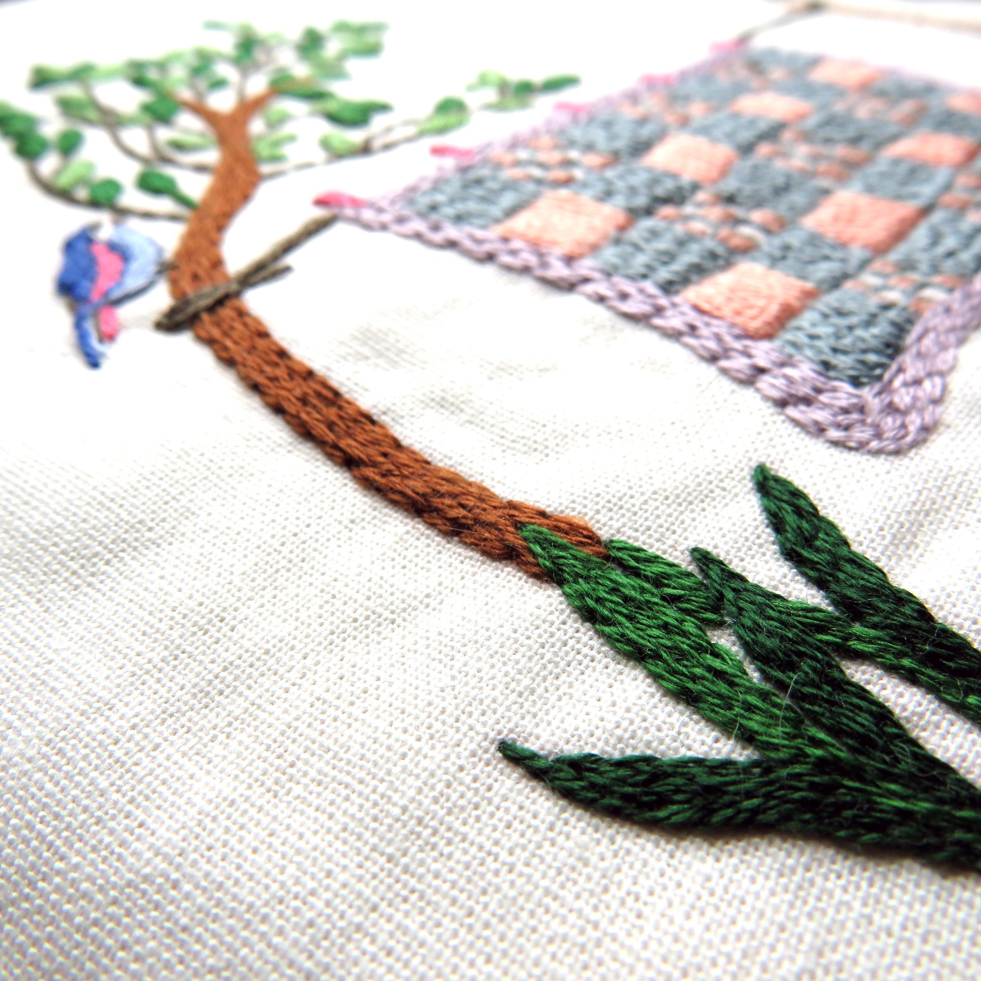 Embroidered scene with a tree, bird, and checkered patch on fabric.