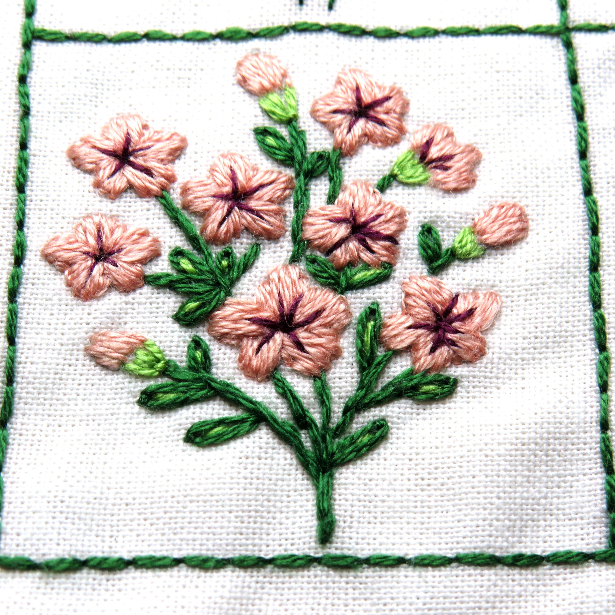 Embroidered design of pink flowers with green leaves on white fabric.