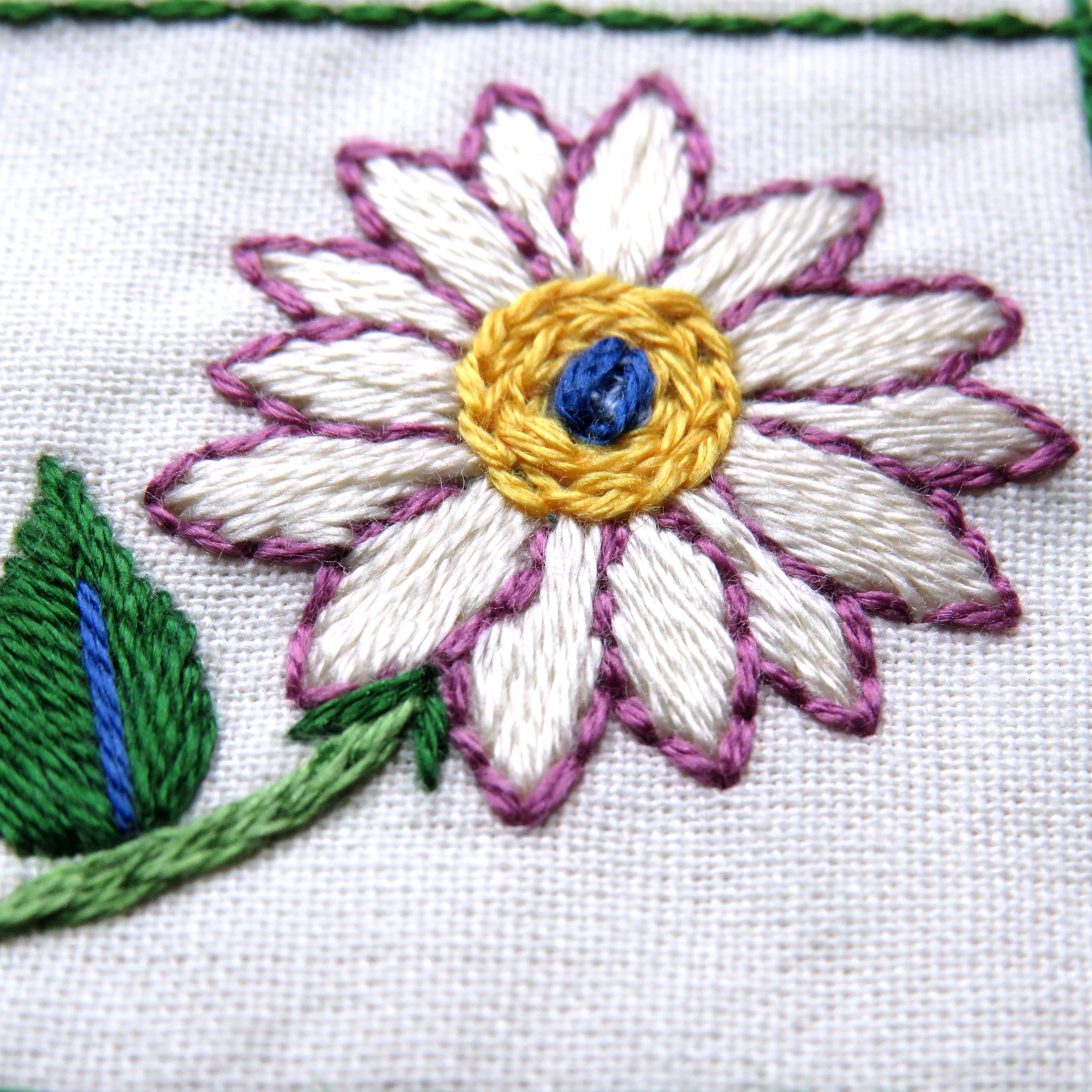 Embroidered flower design on fabric with white, purple, yellow, and green colors.