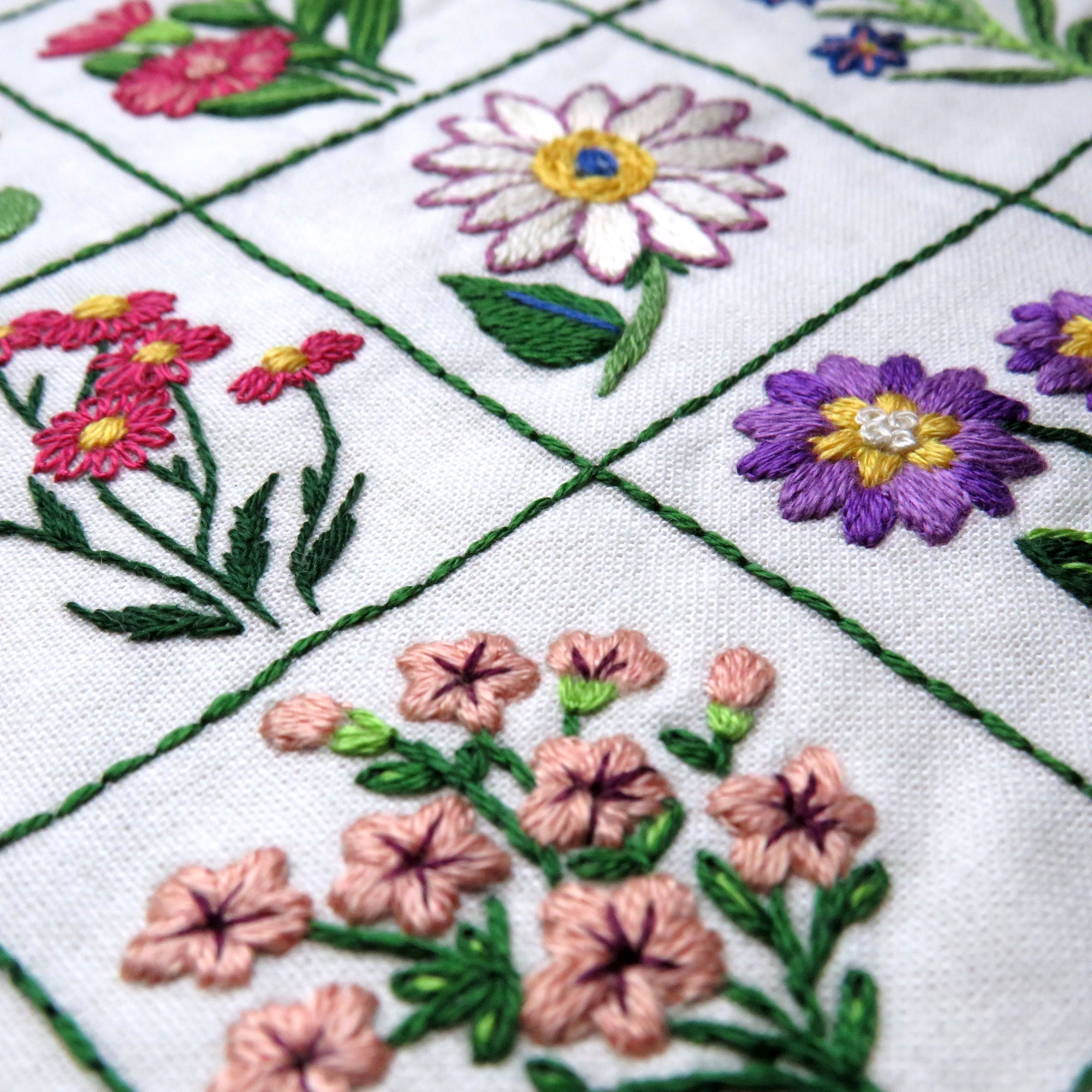 Close-up of embroidered flowers on a quilt with green grid lines.