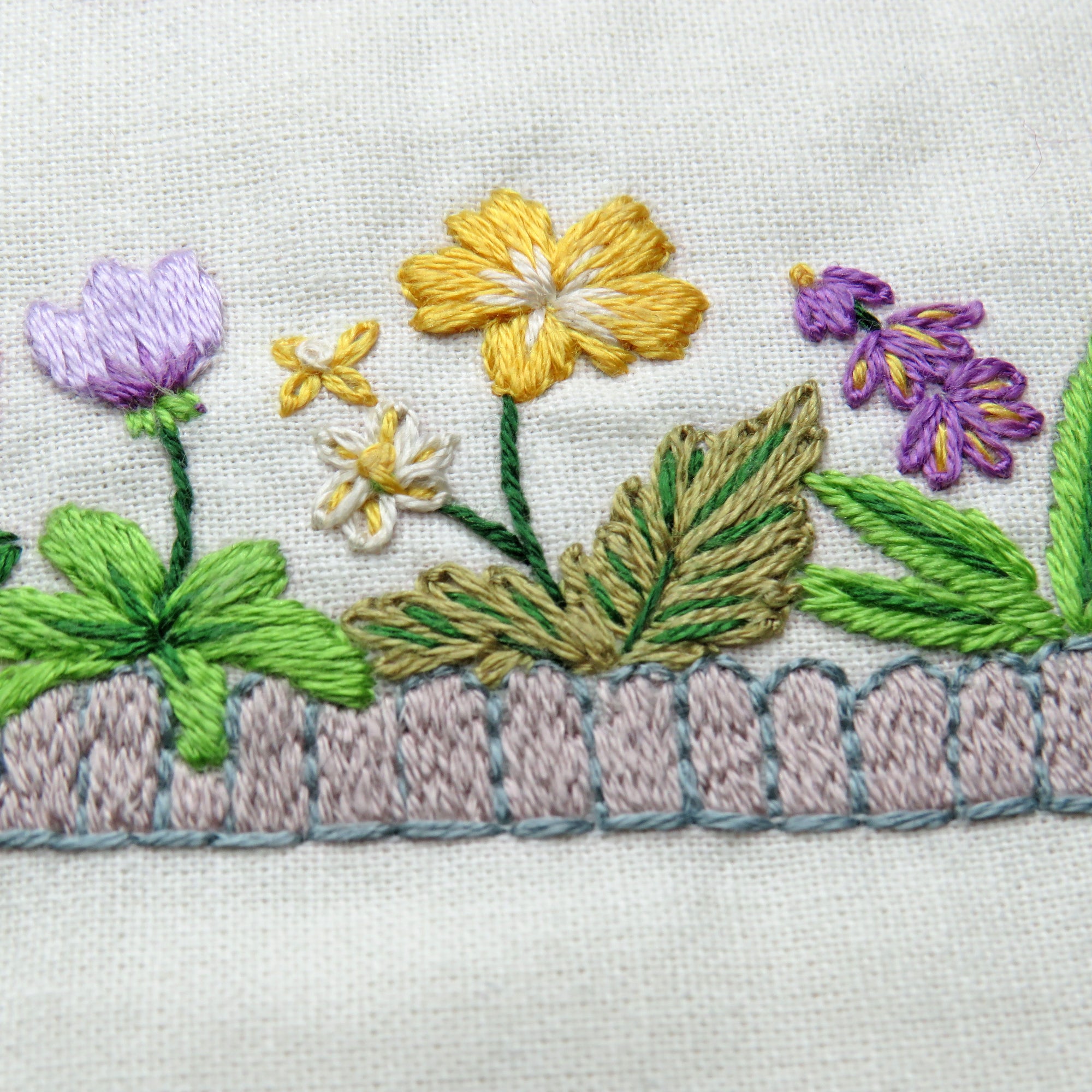 Embroidered floral design on fabric with flowers and leaves.