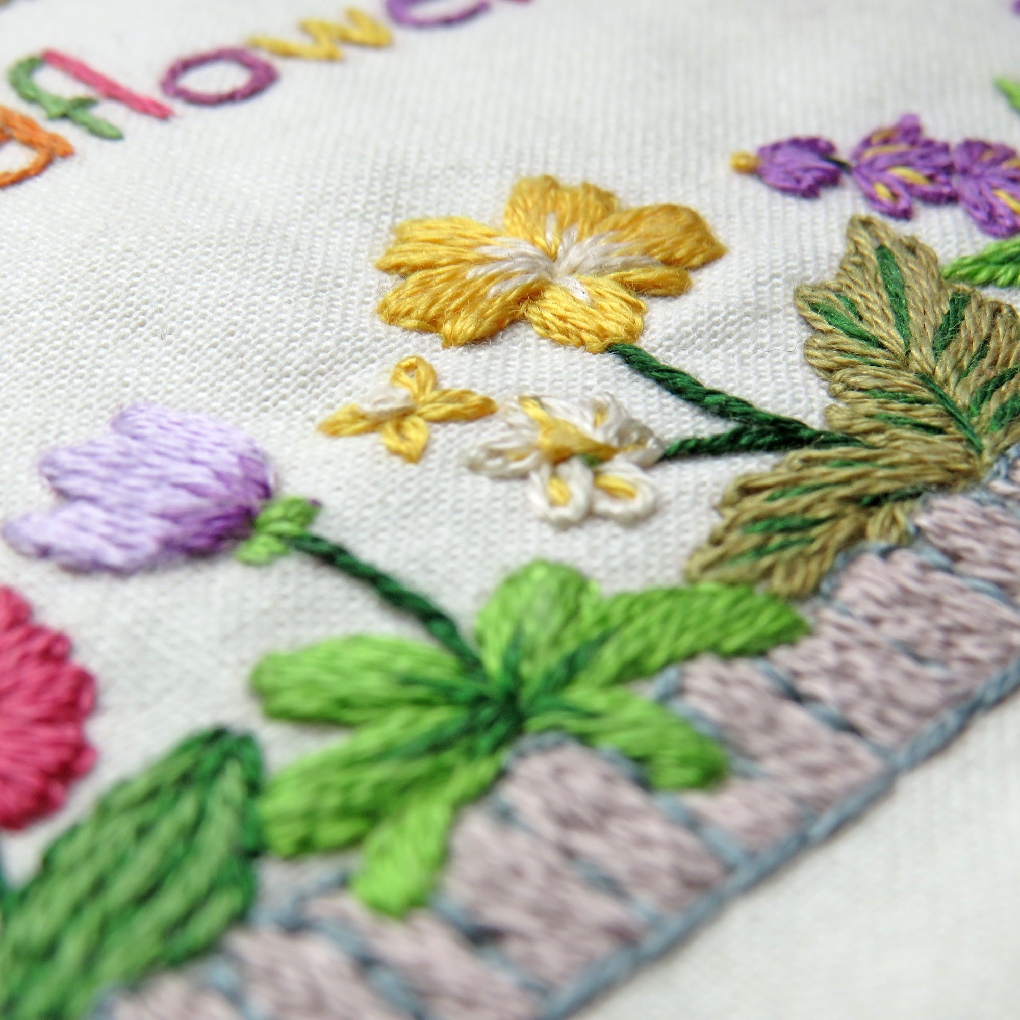 Embroidered floral design with colorful flowers and leaves on a white fabric background.