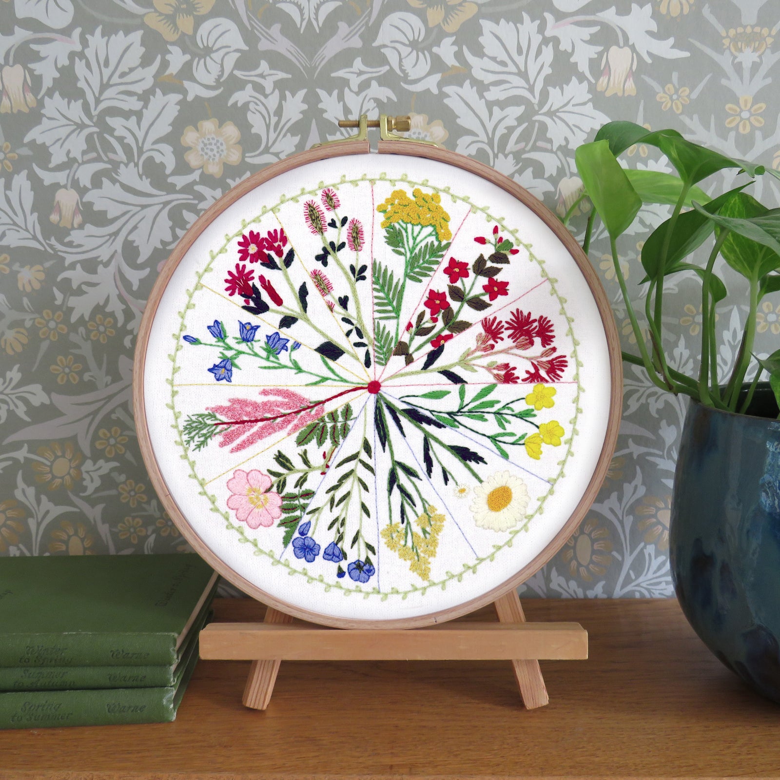 Embroidery hoop with floral design on a wooden stand against a decorative wall.