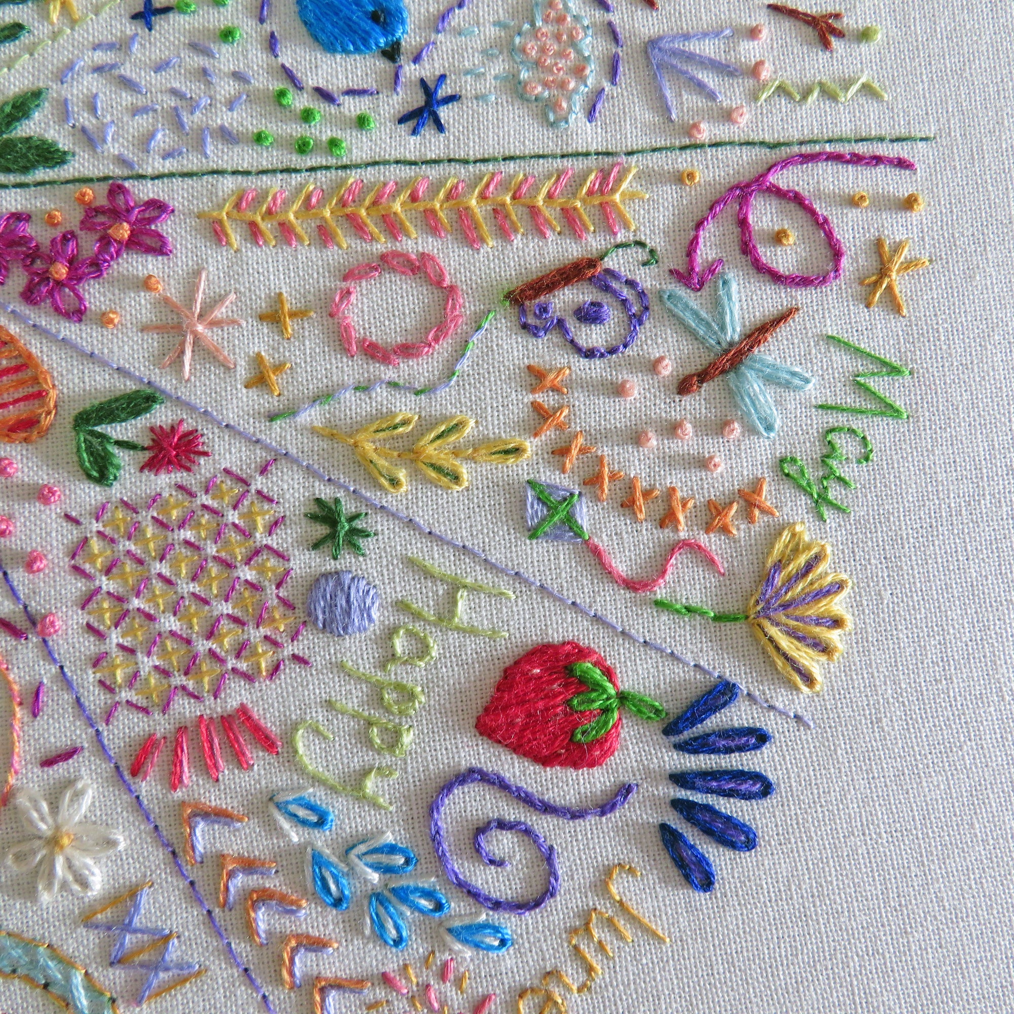 Close-up of a colorful embroidered textile featuring floral motifs, leaves, butterflies, and decorative stitching on a light fabric background.