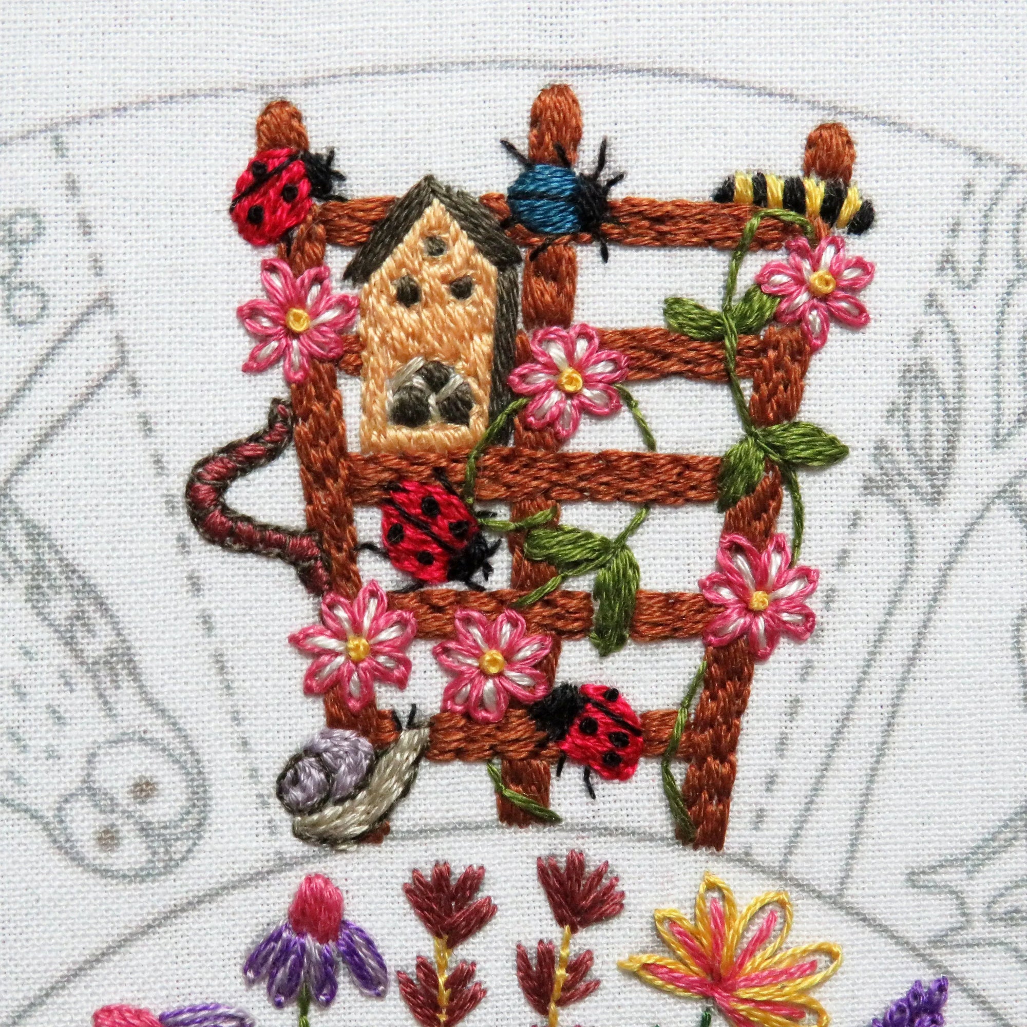 Embroidery design of a birdhouse with flowers and ladybugs on a white background
