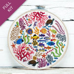 Embroidery hoop with colorful underwater scene including fish, corals, and turtles on a white wooden surface.