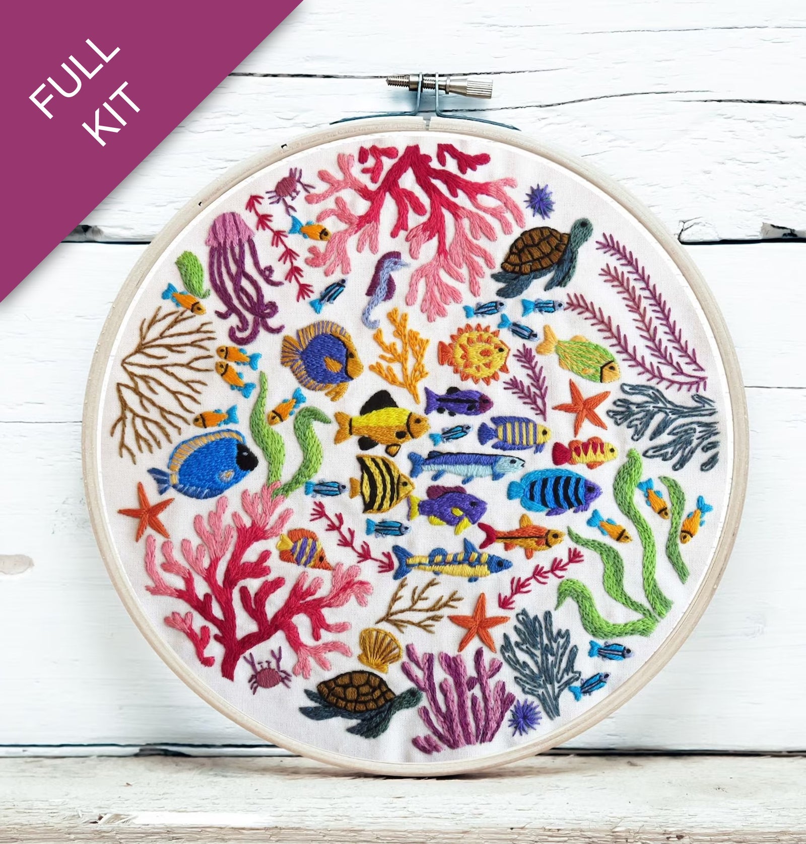 Embroidery hoop with colorful underwater scene including fish, corals, and turtles on a white wooden surface.