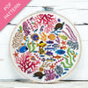 Embroidery hoop with colorful underwater scene including fish, corals, and turtles on a white wooden surface.