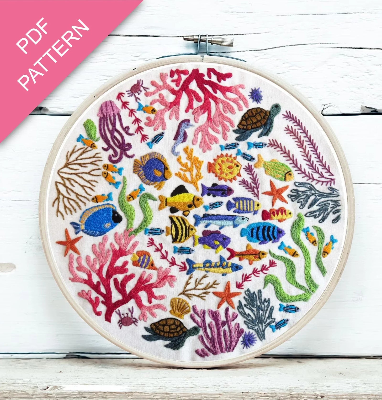 Embroidery hoop with colorful underwater scene including fish, corals, and turtles on a white wooden surface.
