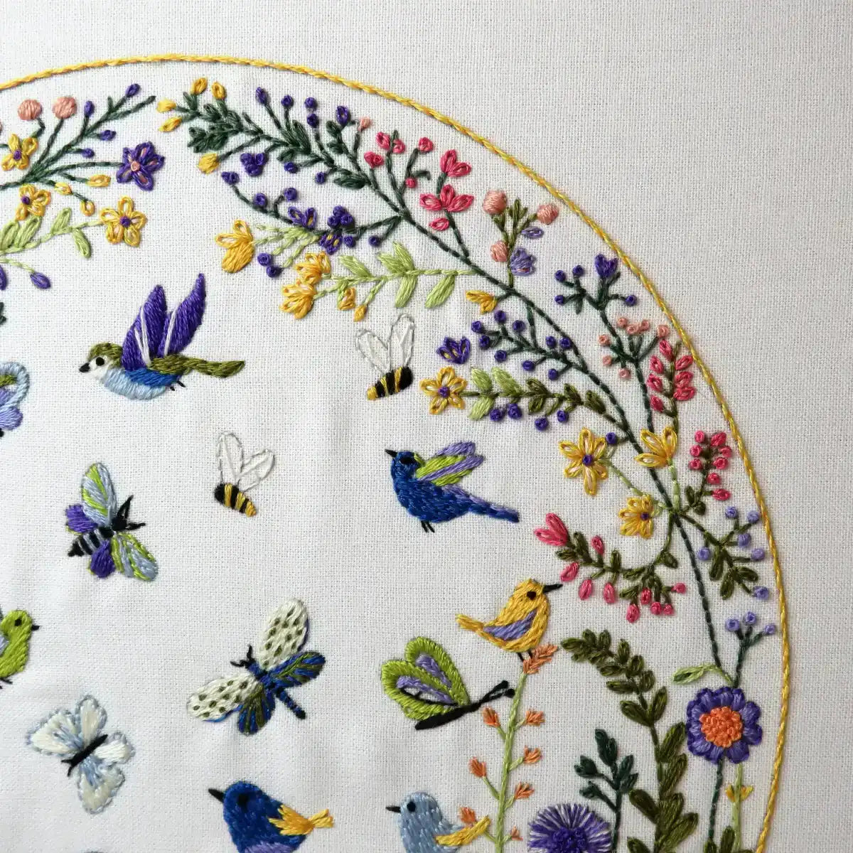 Embroidery hoop with colorful floral and insect design on a white background