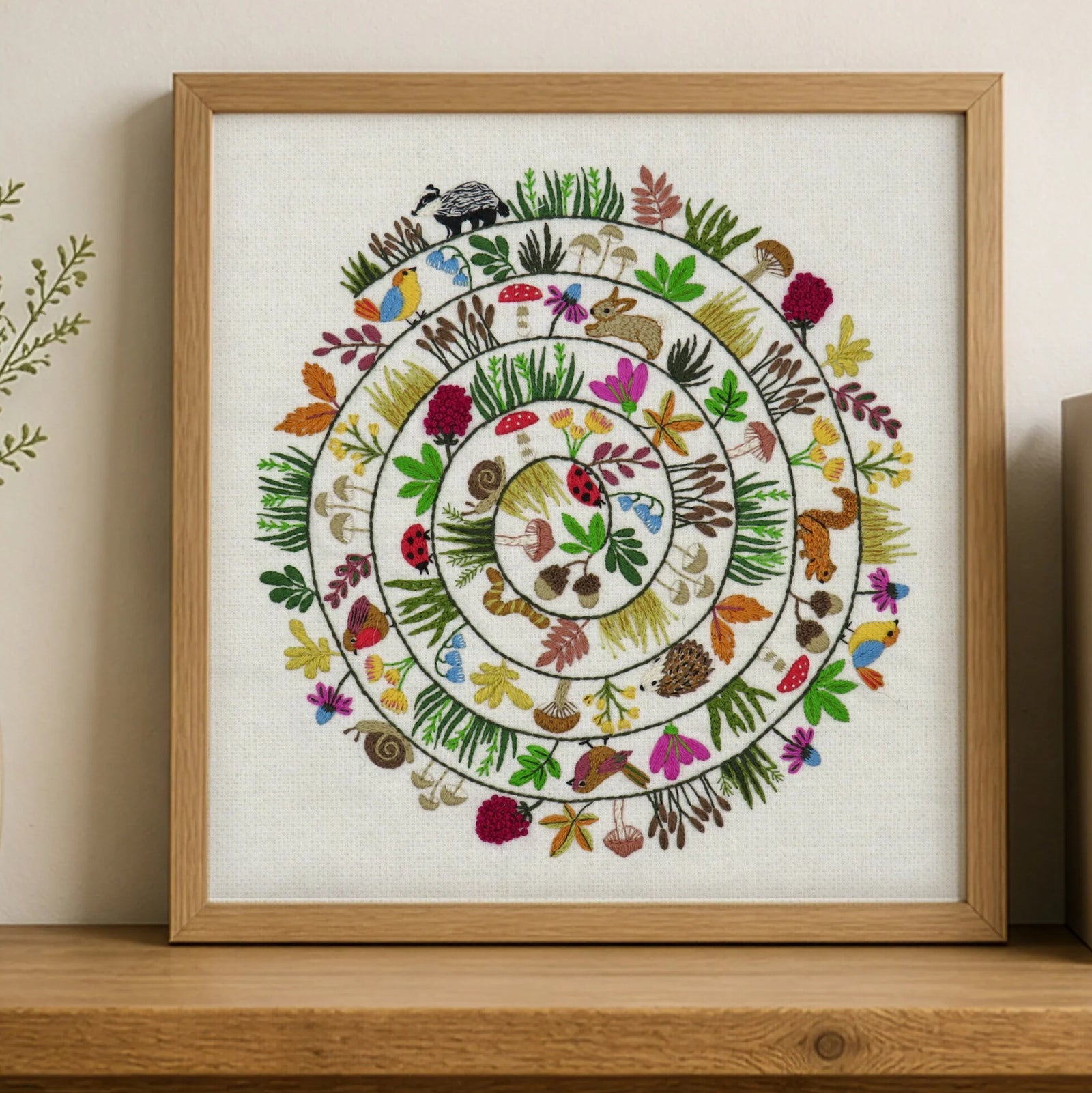 Framed artwork with a colorful circular design of animals and plants on a wooden shelf.