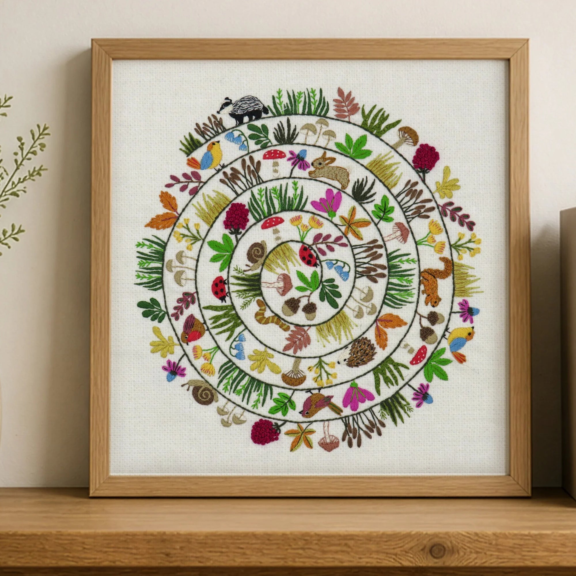Framed artwork with a colorful circular design of animals and plants on a wooden shelf.