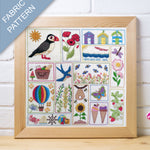 Framed fabric pattern with various designs including a puffin, flowers, and ice cream cones on a wooden surface.