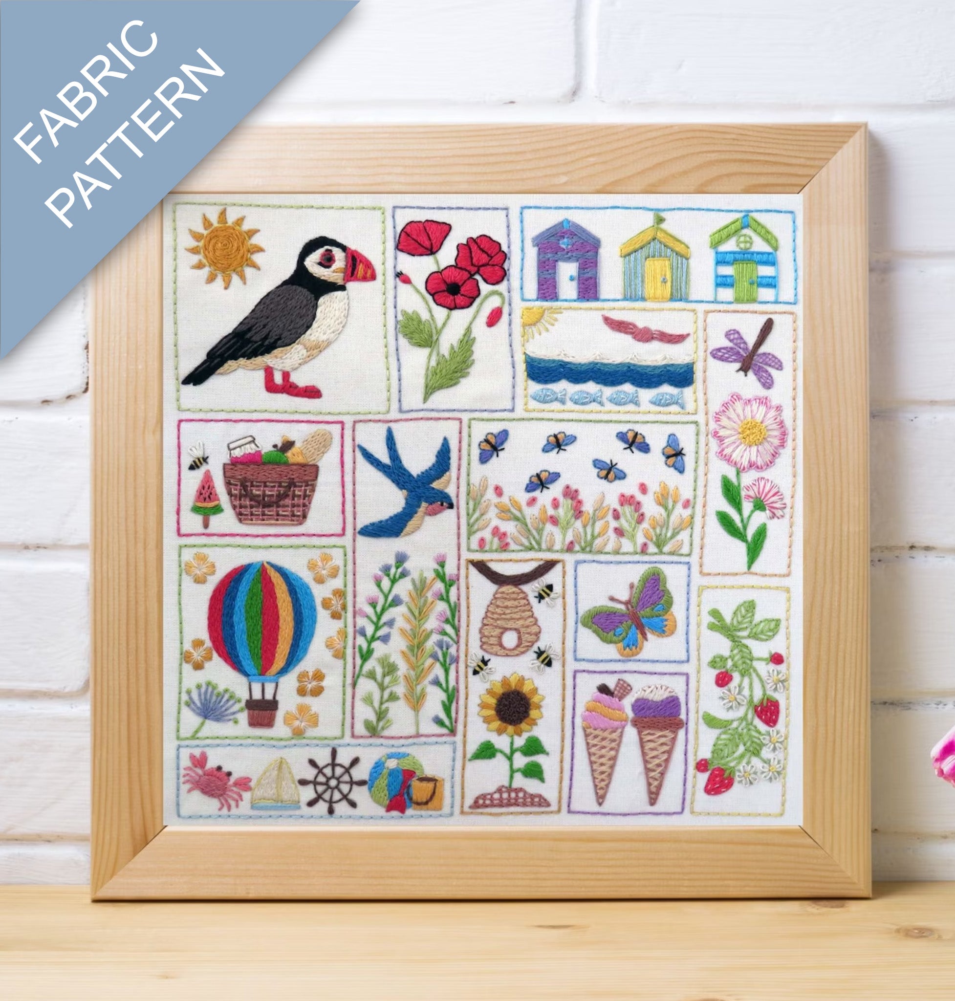 Framed fabric pattern with various designs including a puffin, flowers, and ice cream cones on a wooden surface.