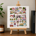 Decorative print of houses and flowers on a small easel with books and a plant in the background.