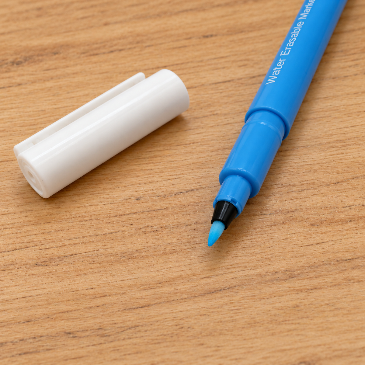 A blue water erase marker with its white cap removed, placed on a light brown wooden surface.