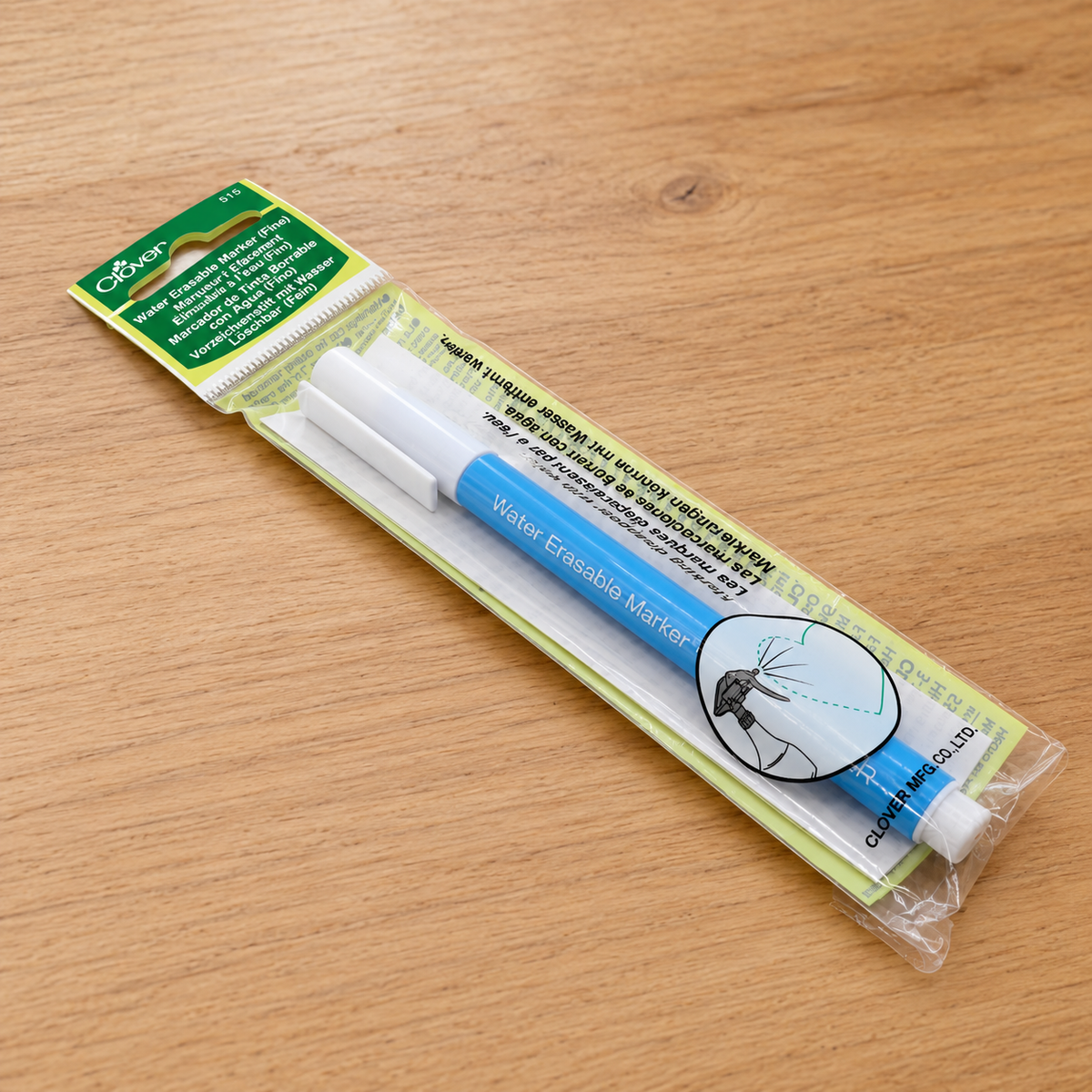 A packaged water fountain pen with a blue barrel, white cap and tip, and a green-and-white header card, photographed on a light wood tabletop.