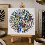 Colorful mandala painting on a small easel with a cup of coffee, notebook, and lamp in the background.