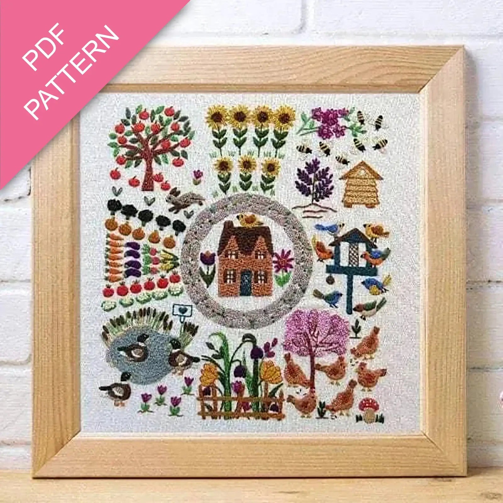Framed embroidered artwork with a house and garden design on a white background