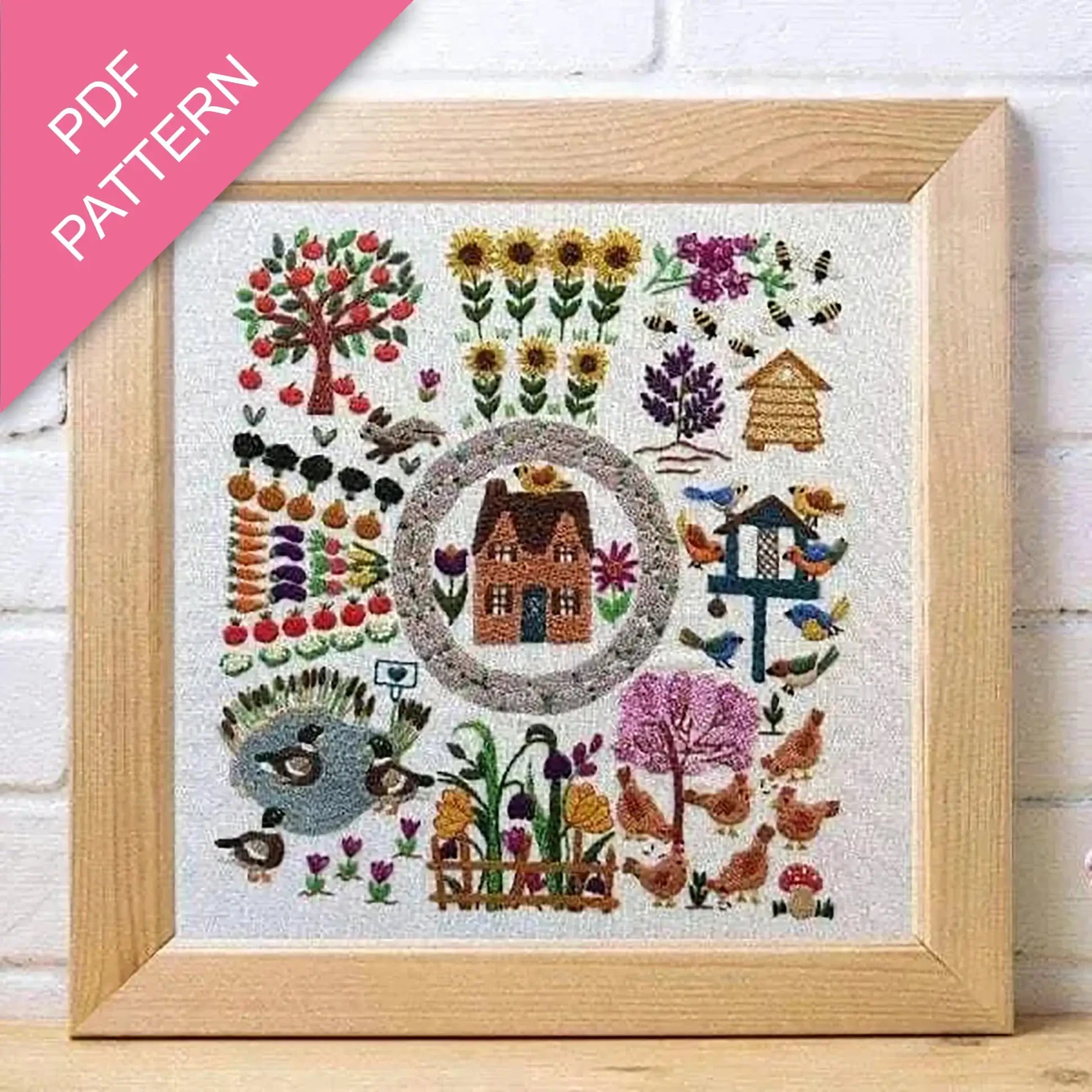 Framed embroidered artwork with a house and garden design on a white background