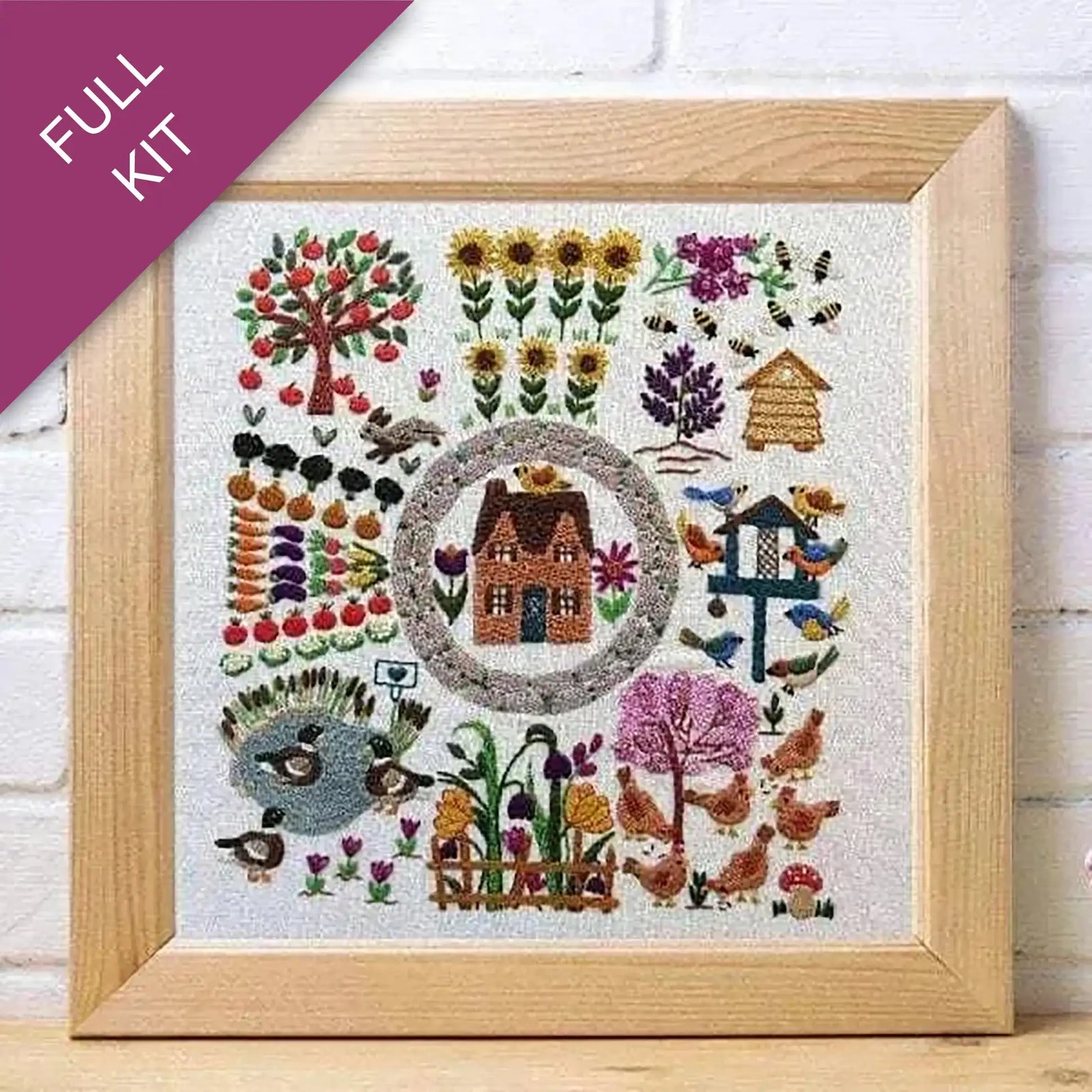 Framed embroidered artwork with a house, trees, flowers, and animals on a white background.