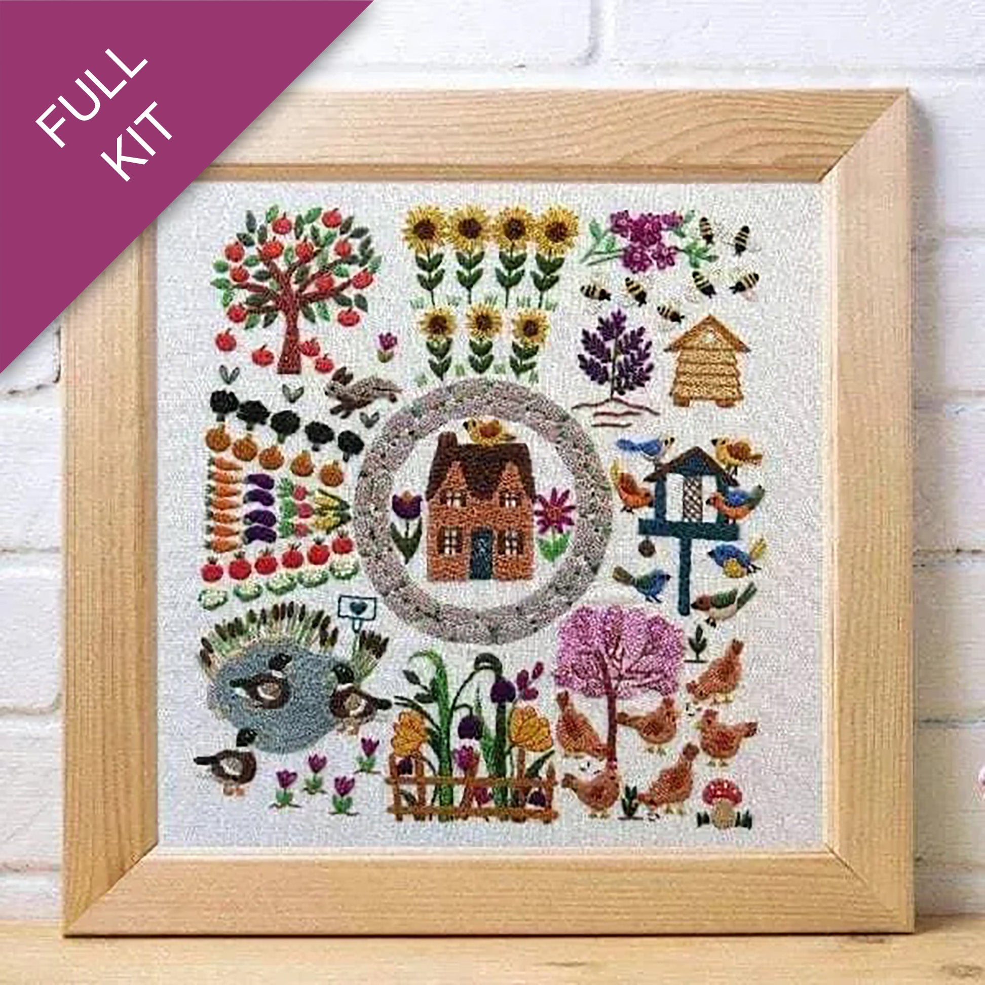 Framed embroidered artwork with a house, trees, flowers, and animals on a white background.
