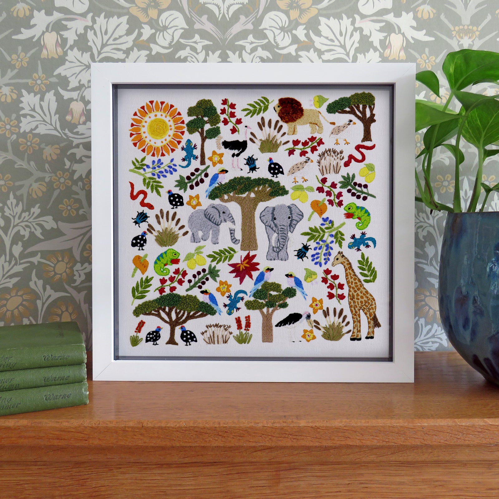 Framed artwork with colorful animals and nature elements on a wooden surface.